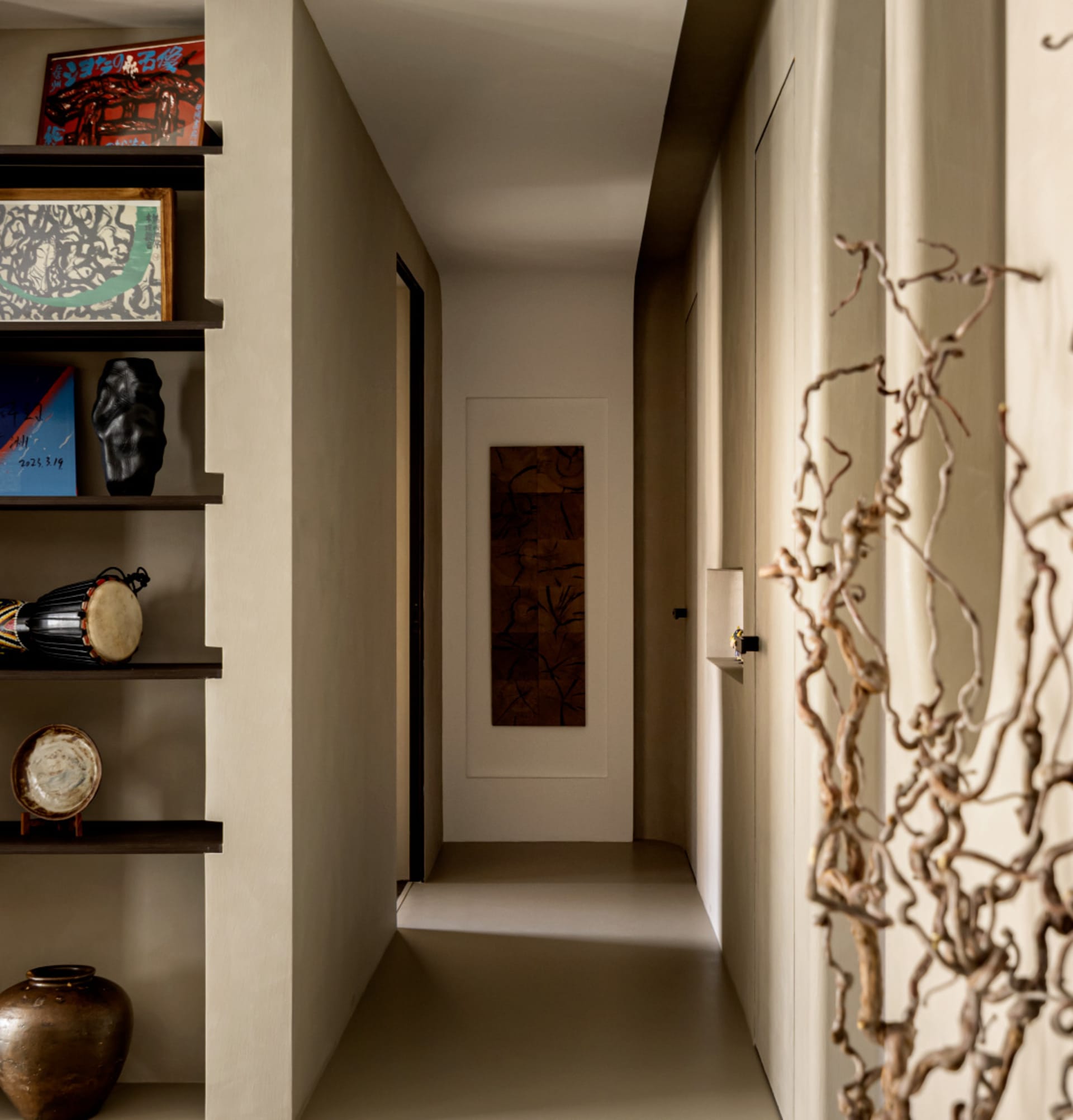 A modern, minimalist corridor with neutral-toned walls and floors, decorated with a few art pieces and a wooden wall panel.