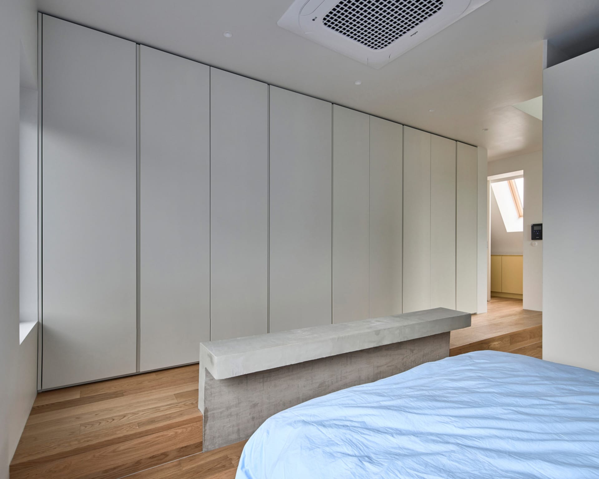 A minimalist bedroom features a concrete bed frame and sleek, white wardrobes.