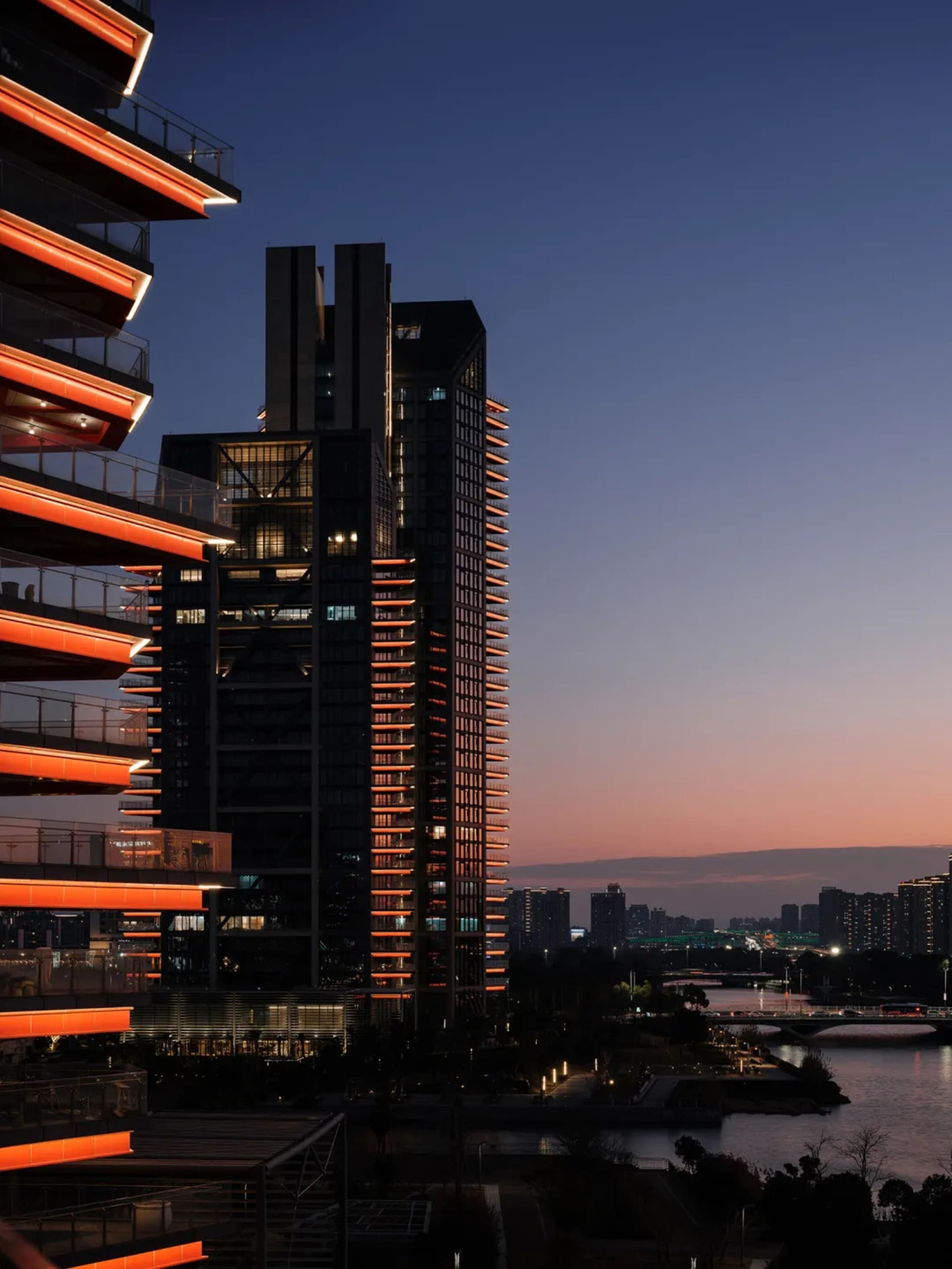 Modern cityscape featuring a tall glass and concrete skyscraper at dusk.