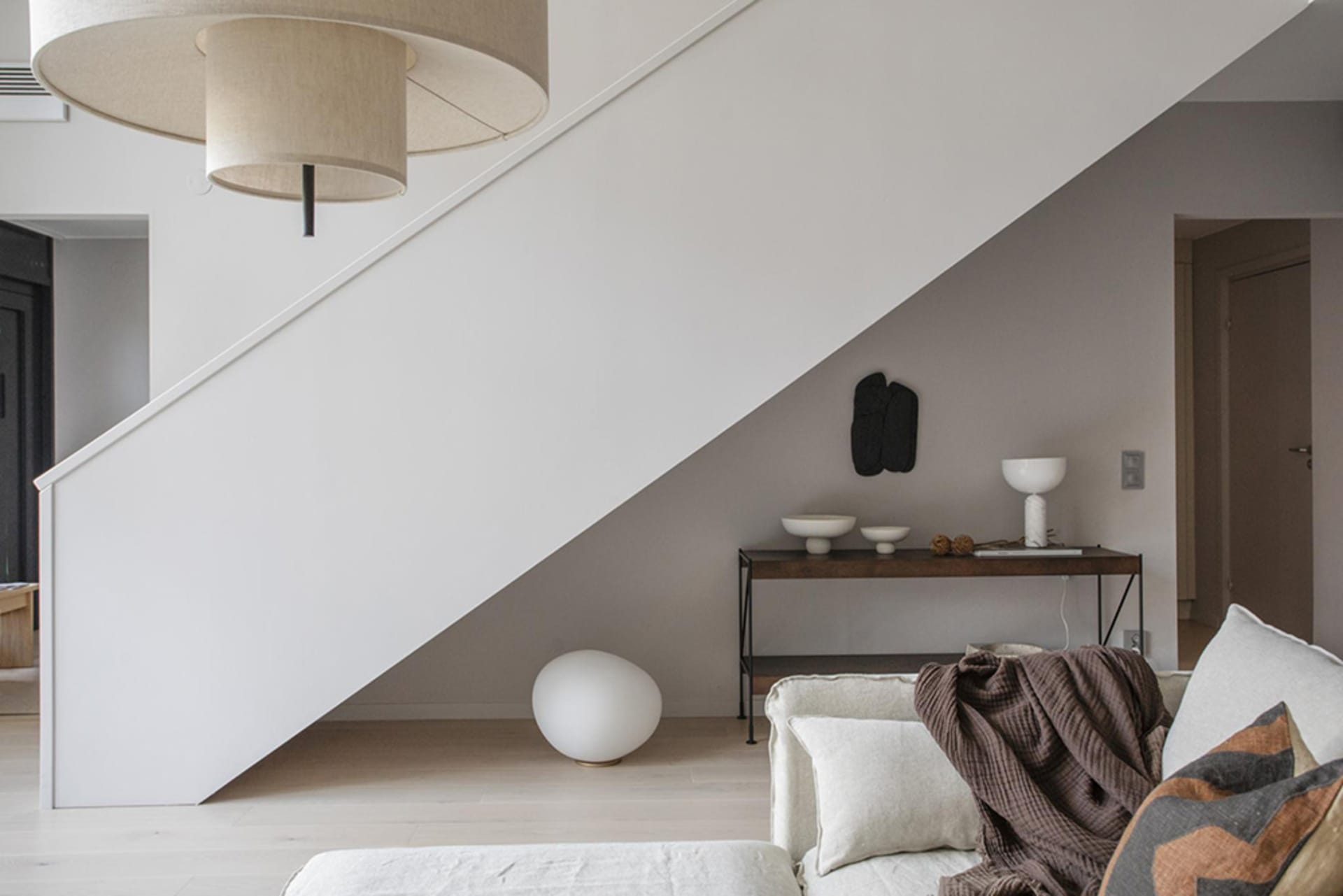 A modern minimalistic living room with neutral tones, showcasing a white sofa, a wooden console table, and a combination of g