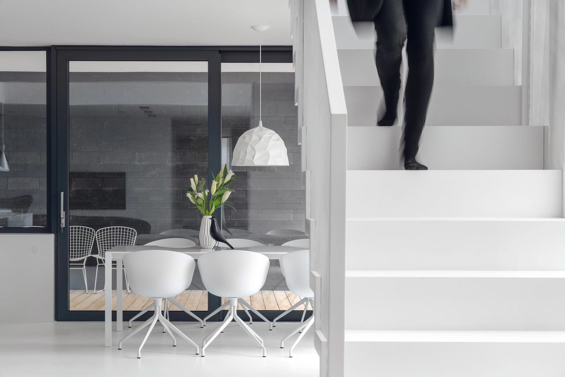 Modern minimalist staircase with concrete steps and a dining area with white chairs and a geometric pendant light.