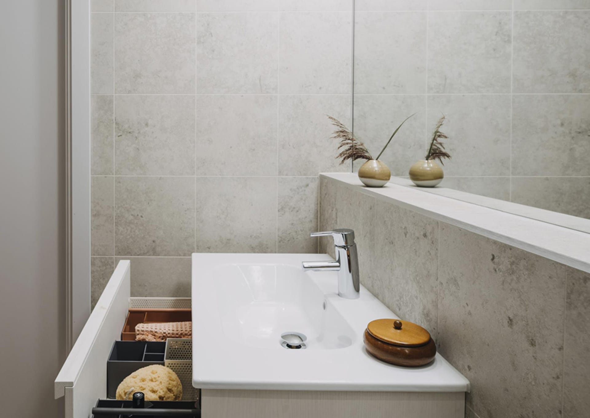 A modern bathroom with concrete walls, minimalist design, and a sleek white sink with a faucet. Decorative vases and a wooden