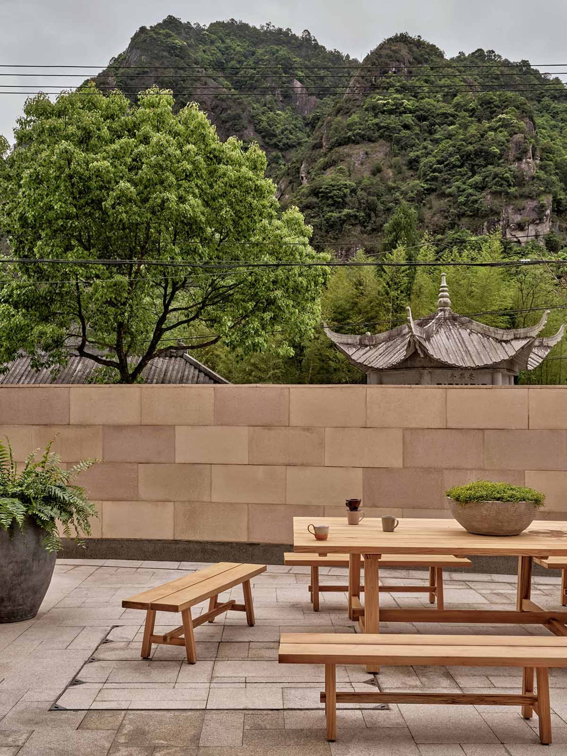 Outdoor seating area with wooden benches and tables overlooking lush greenery and mountains