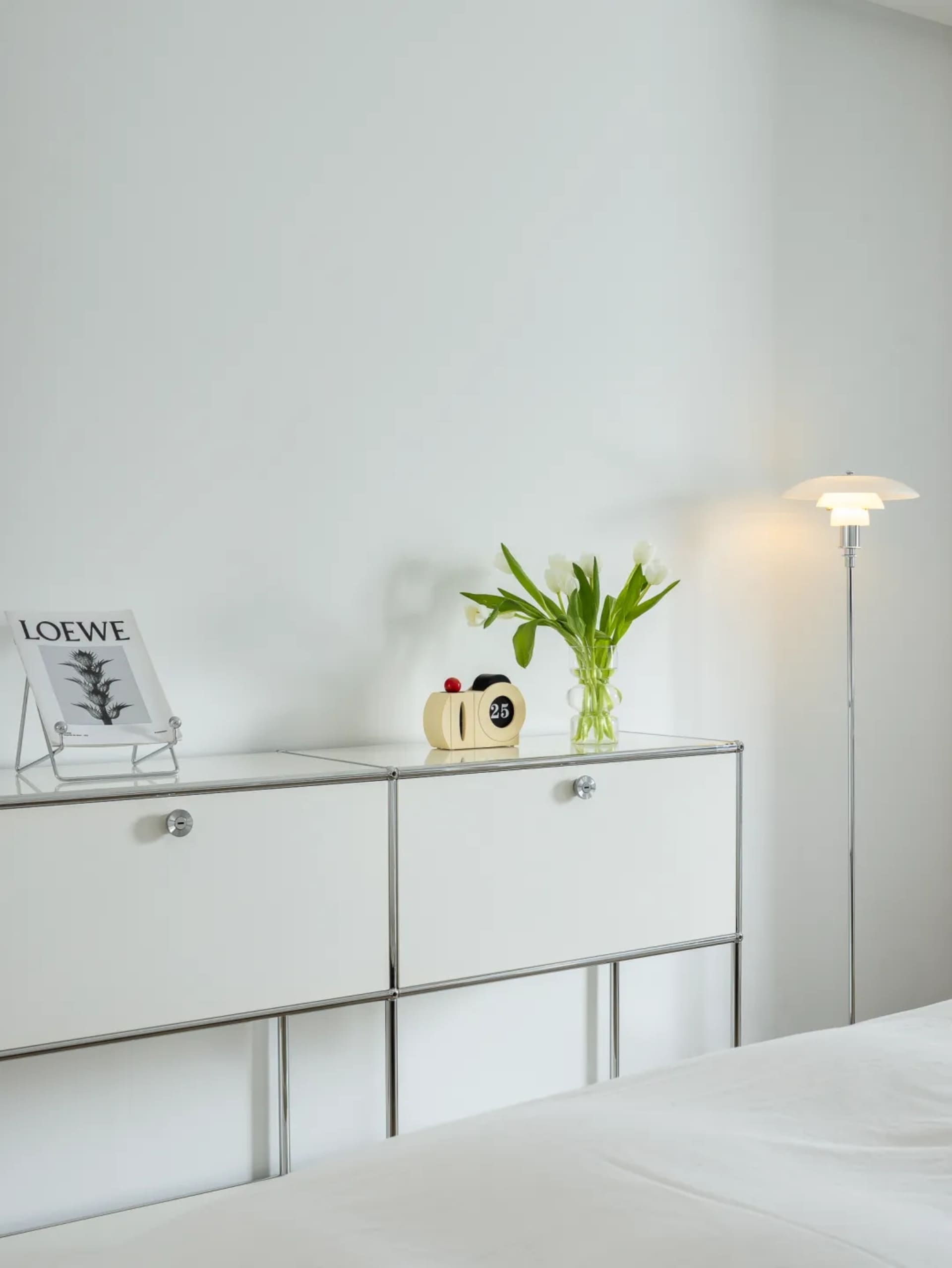 A minimalist bedroom featuring a glass cabinet, white tulips, and a floor lamp.