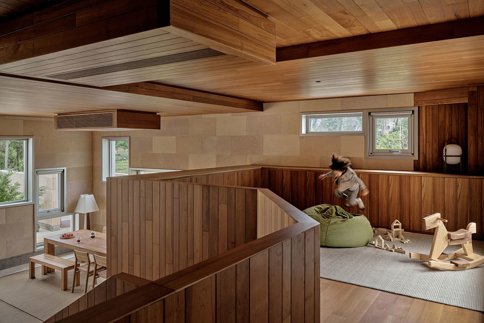 A modern playroom with wooden walls and flooring, featuring a child jumping on a bean bag.