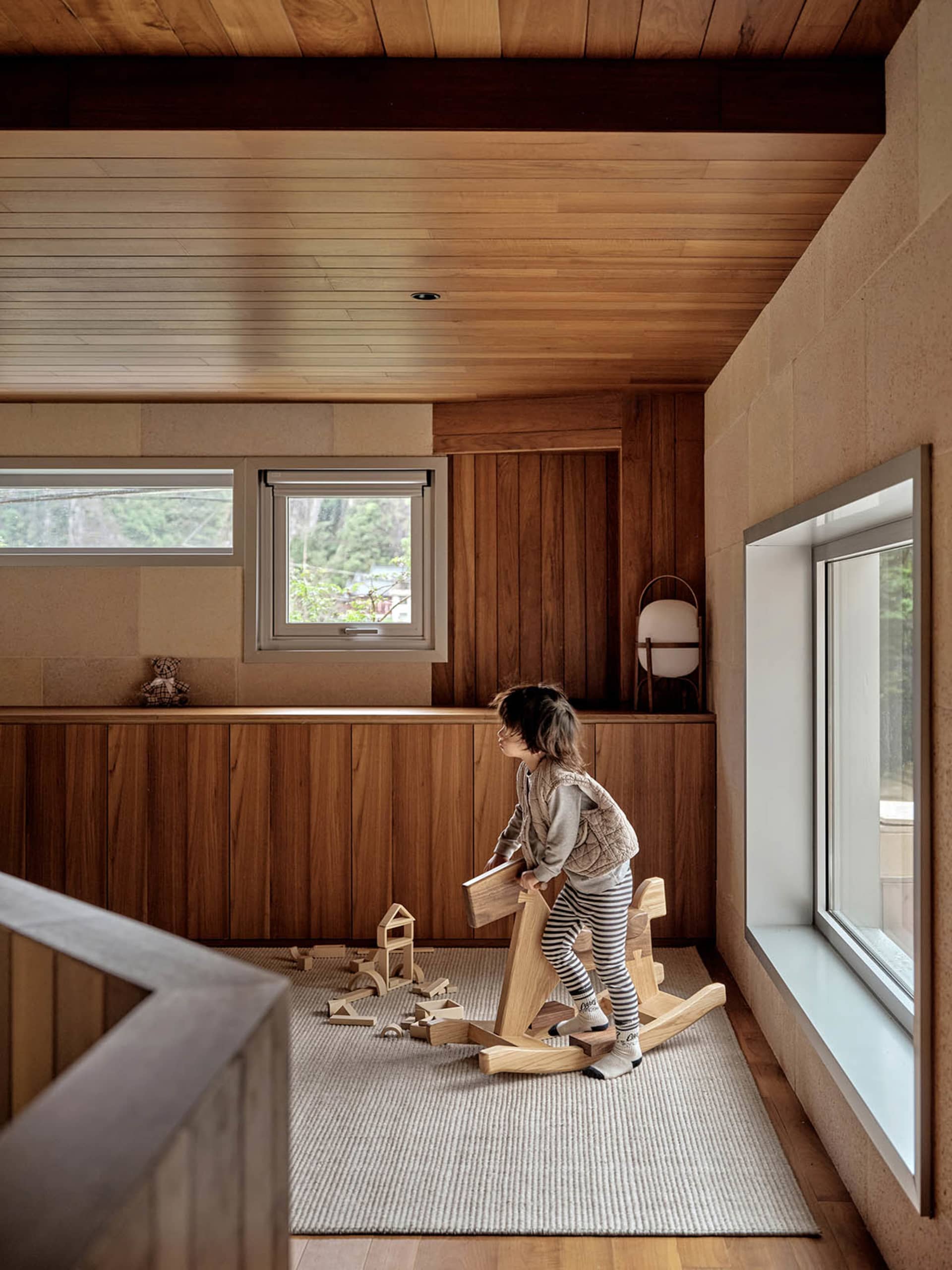 A child playing with building blocks in a modern playroom with wooden flooring and walls.