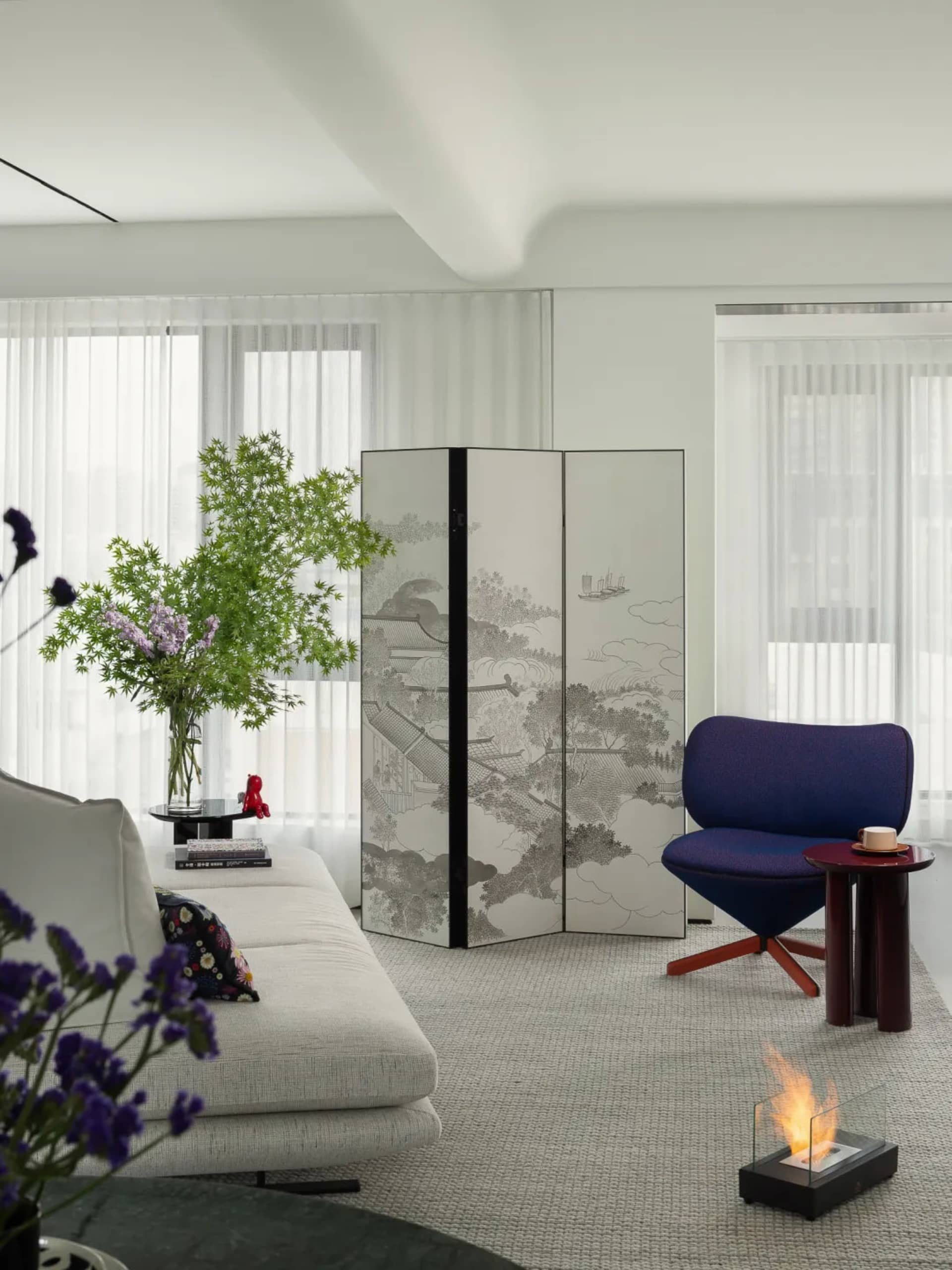 A minimalist living room with a modern decor featuring a white sofa, a purple armchair, a decorative partition, and a glass f
