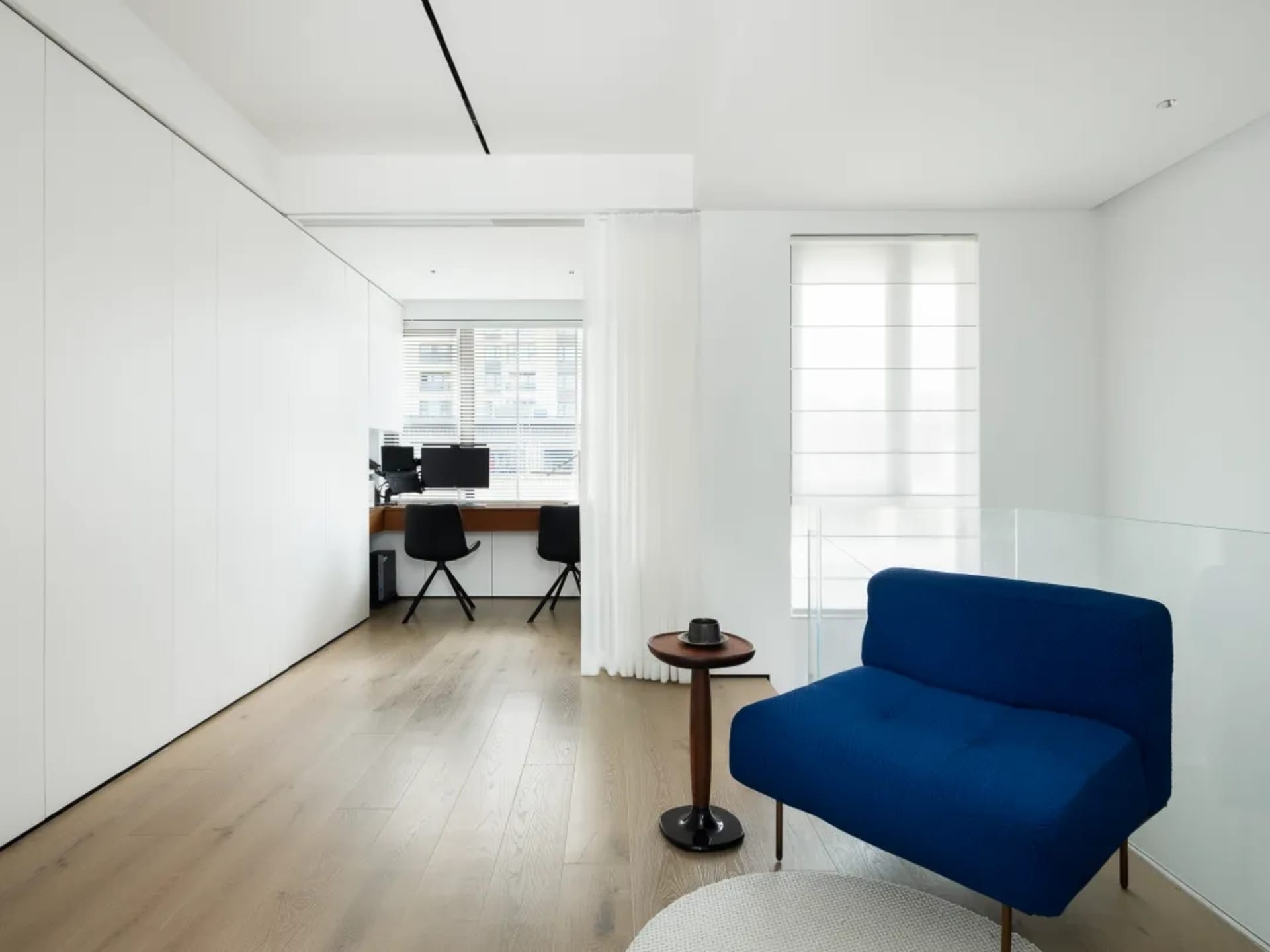 Modern living room with wooden floor, fabric seating, and glass windows