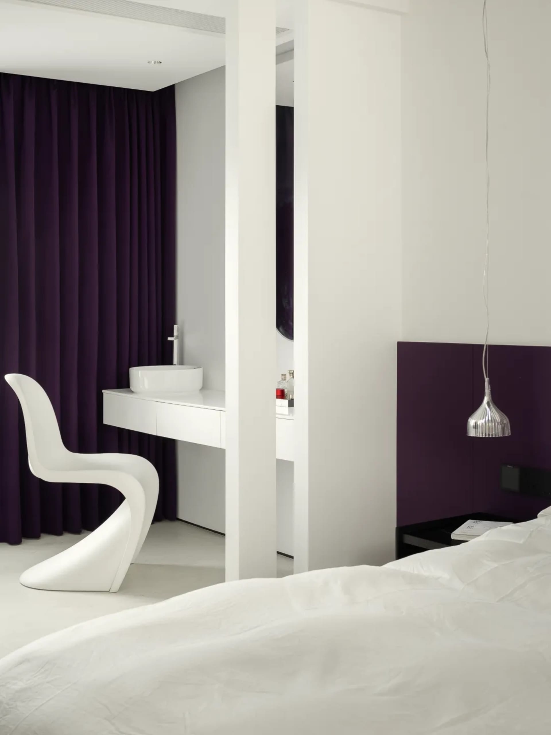 A modern bedroom with white wood flooring, purple accents, and a sleek, white chair.