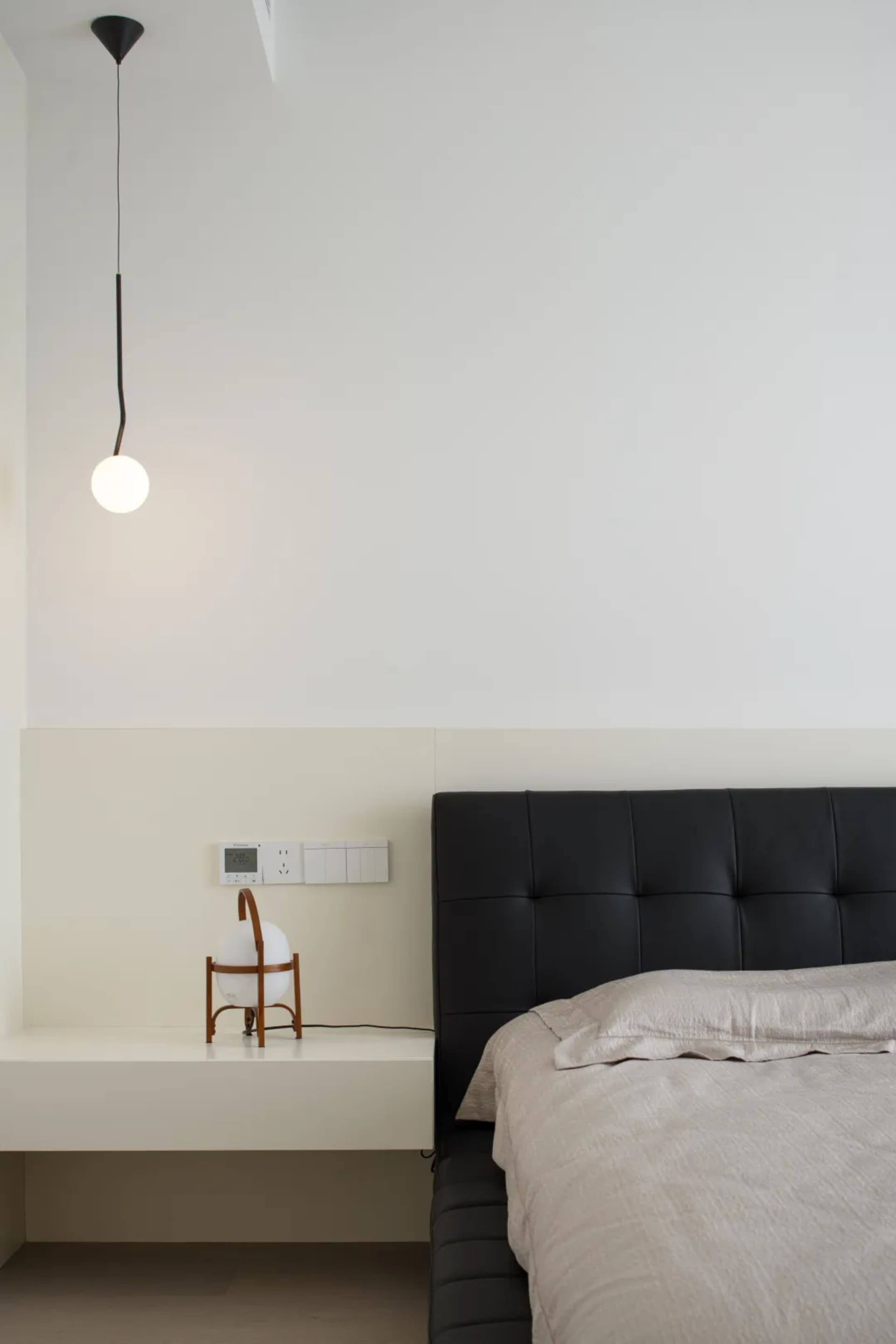 A minimalist bedroom featuring a black leather headboard and light-colored bedding.