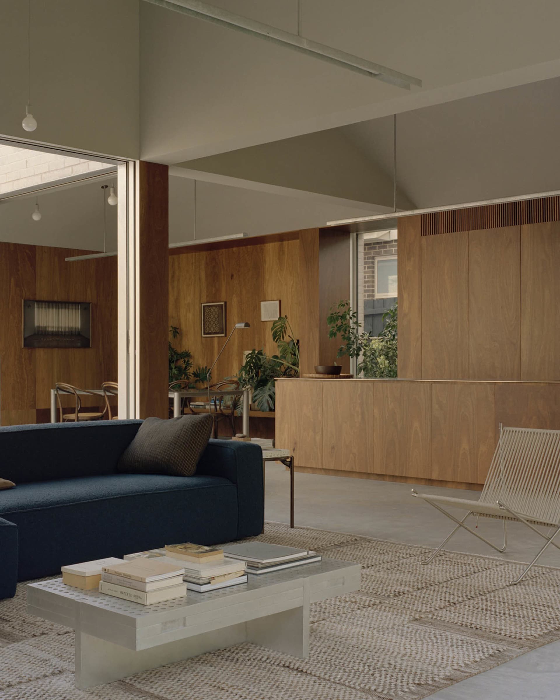 A minimalist living room with wooden walls, blue couch, and white coffee table.