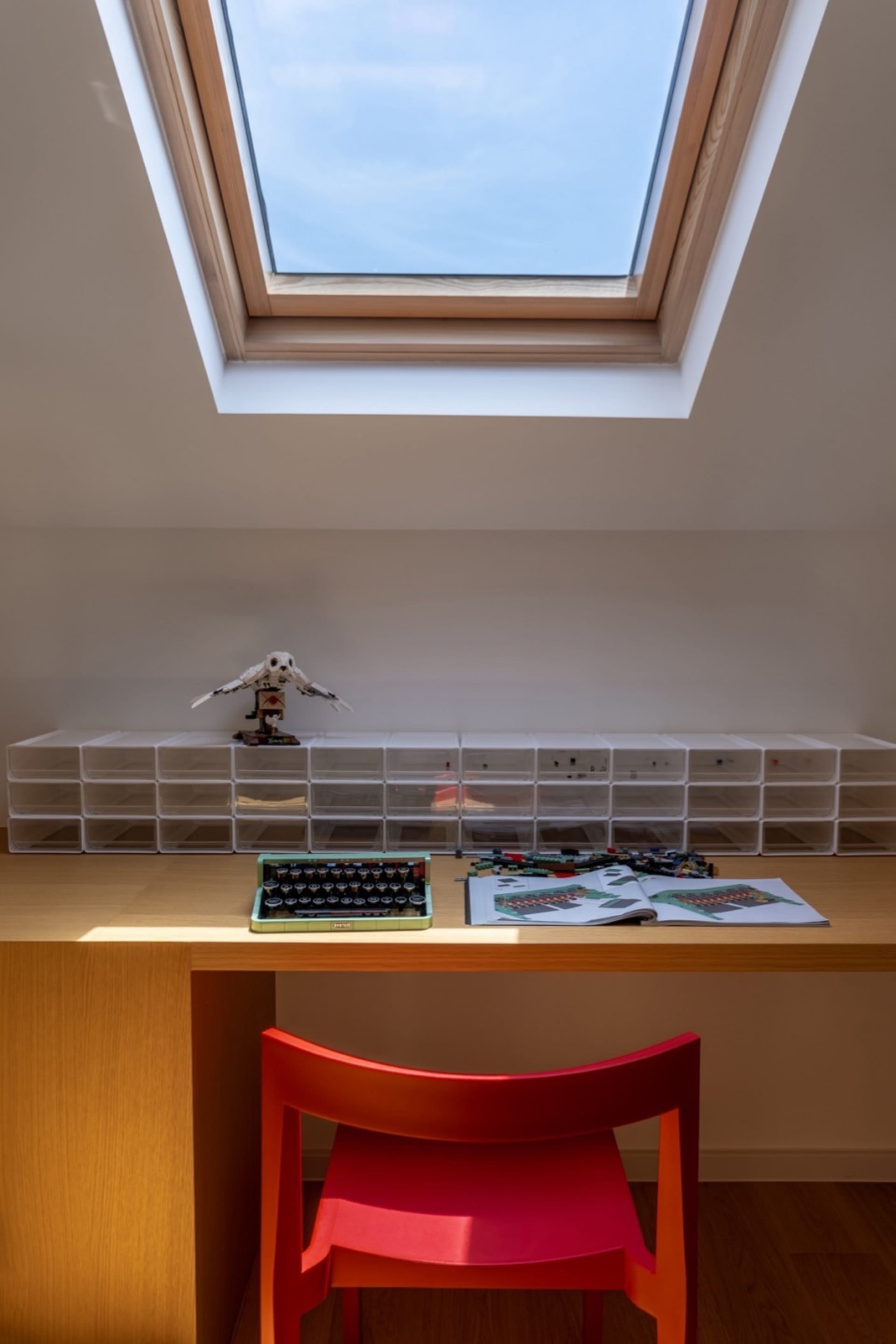 A minimalist study with a wooden desk, a red chair, and a skylight providing natural light.