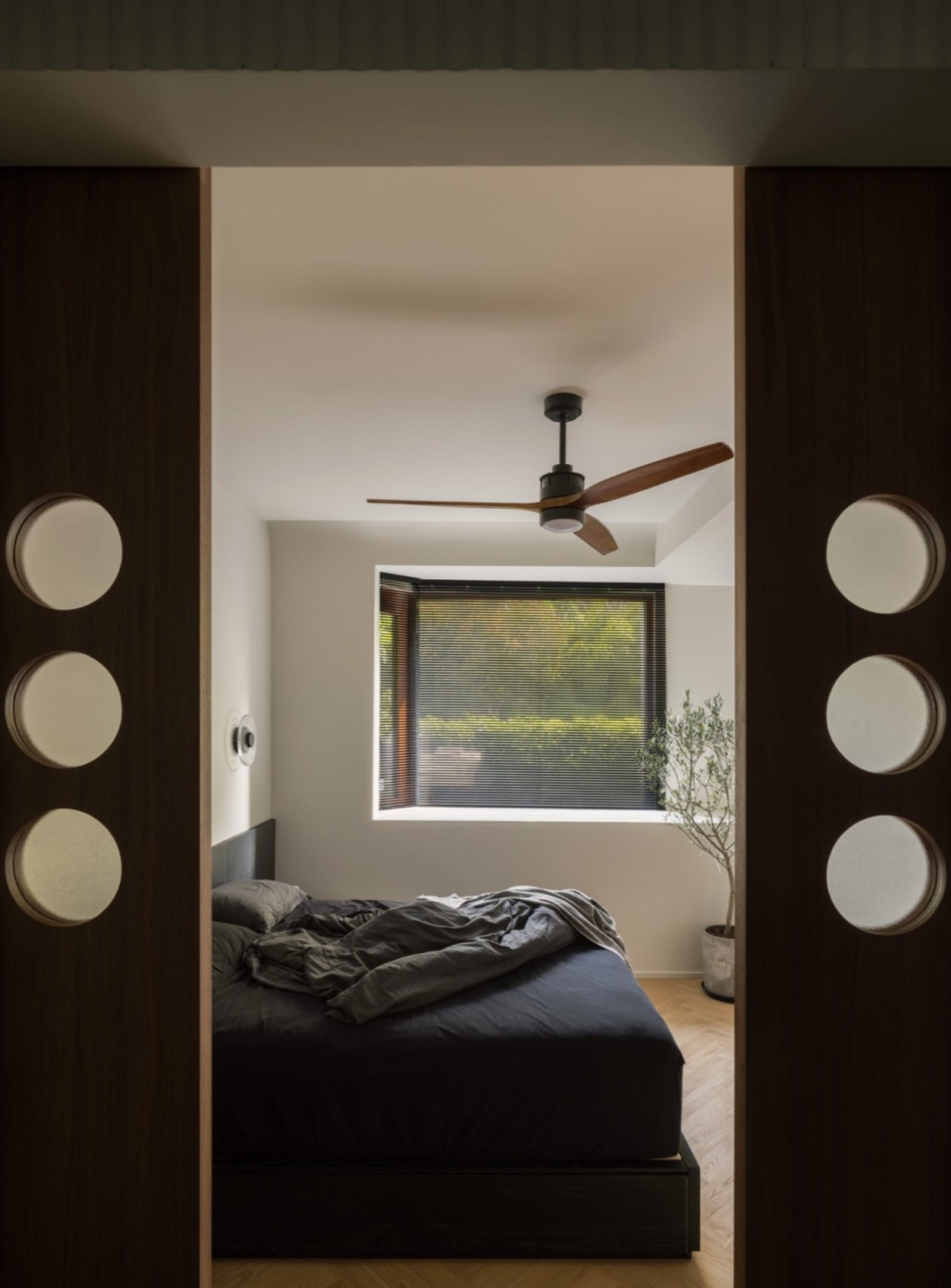A modern bedroom with a dark wood headboard and ceiling fan.