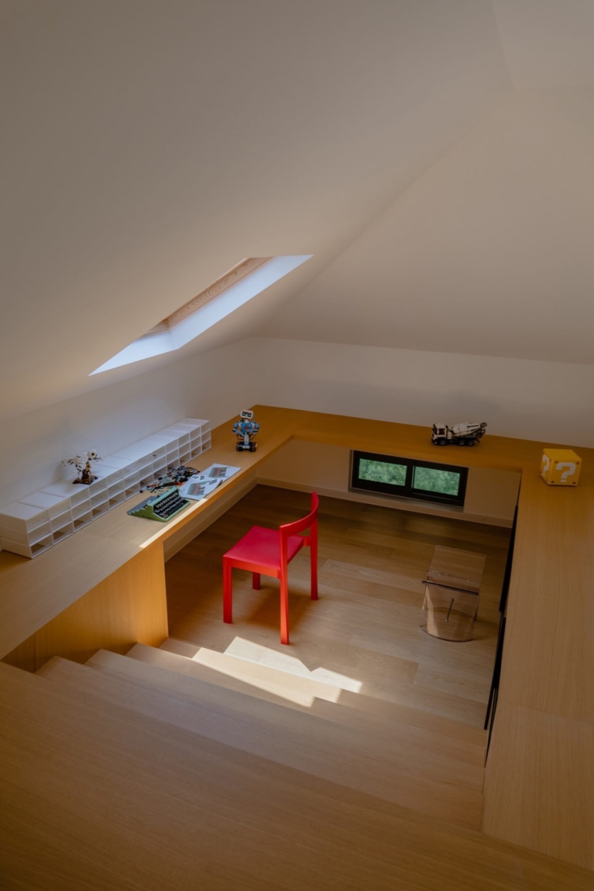 An image of a modern office space featuring a wooden desk and a red chair with a skylight above.