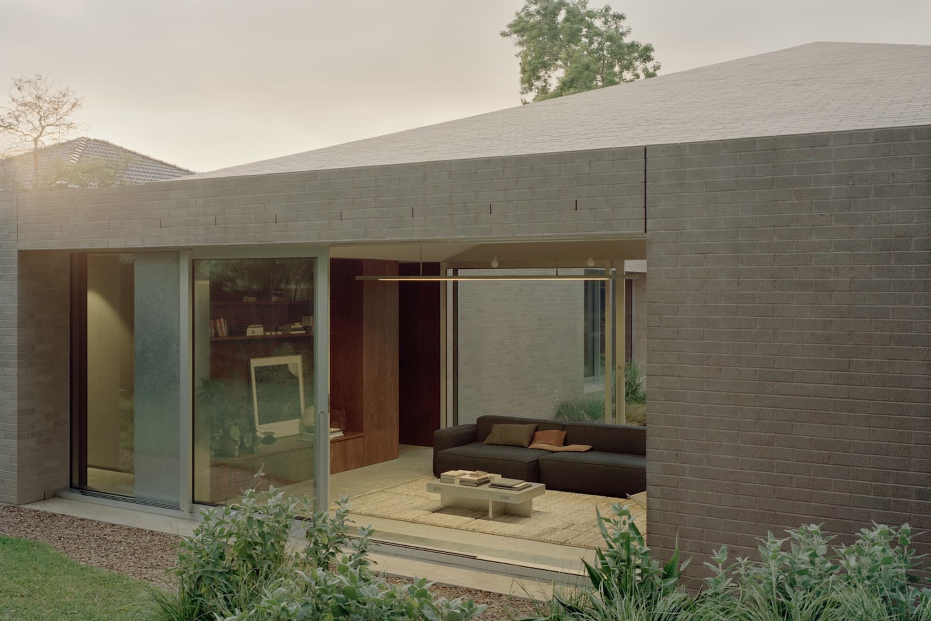 A modern residential exterior featuring a living room with brick, concrete, and glass materials.