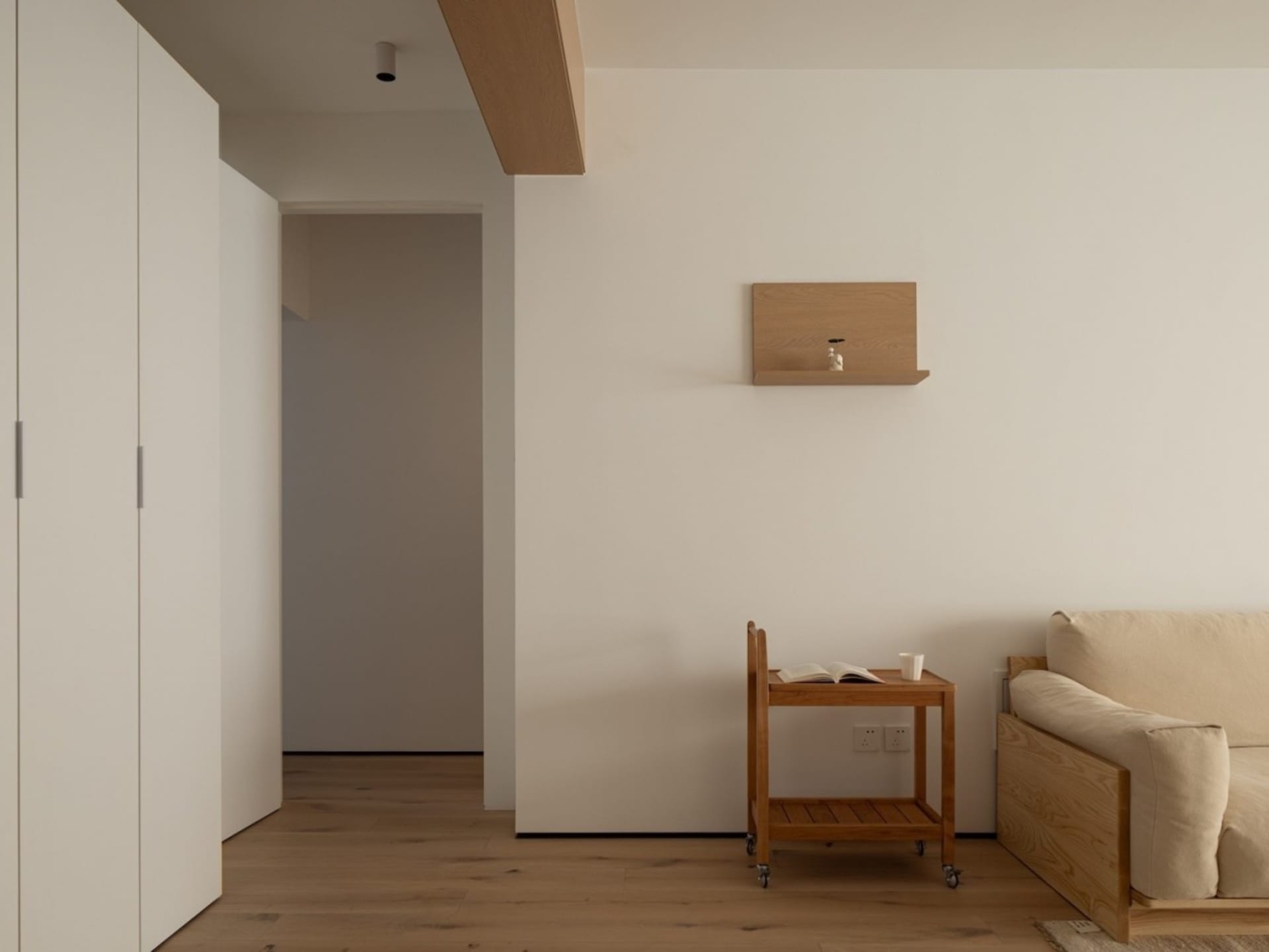 A minimalist residential interior featuring a light-colored wood floor, sofa, and shelves.