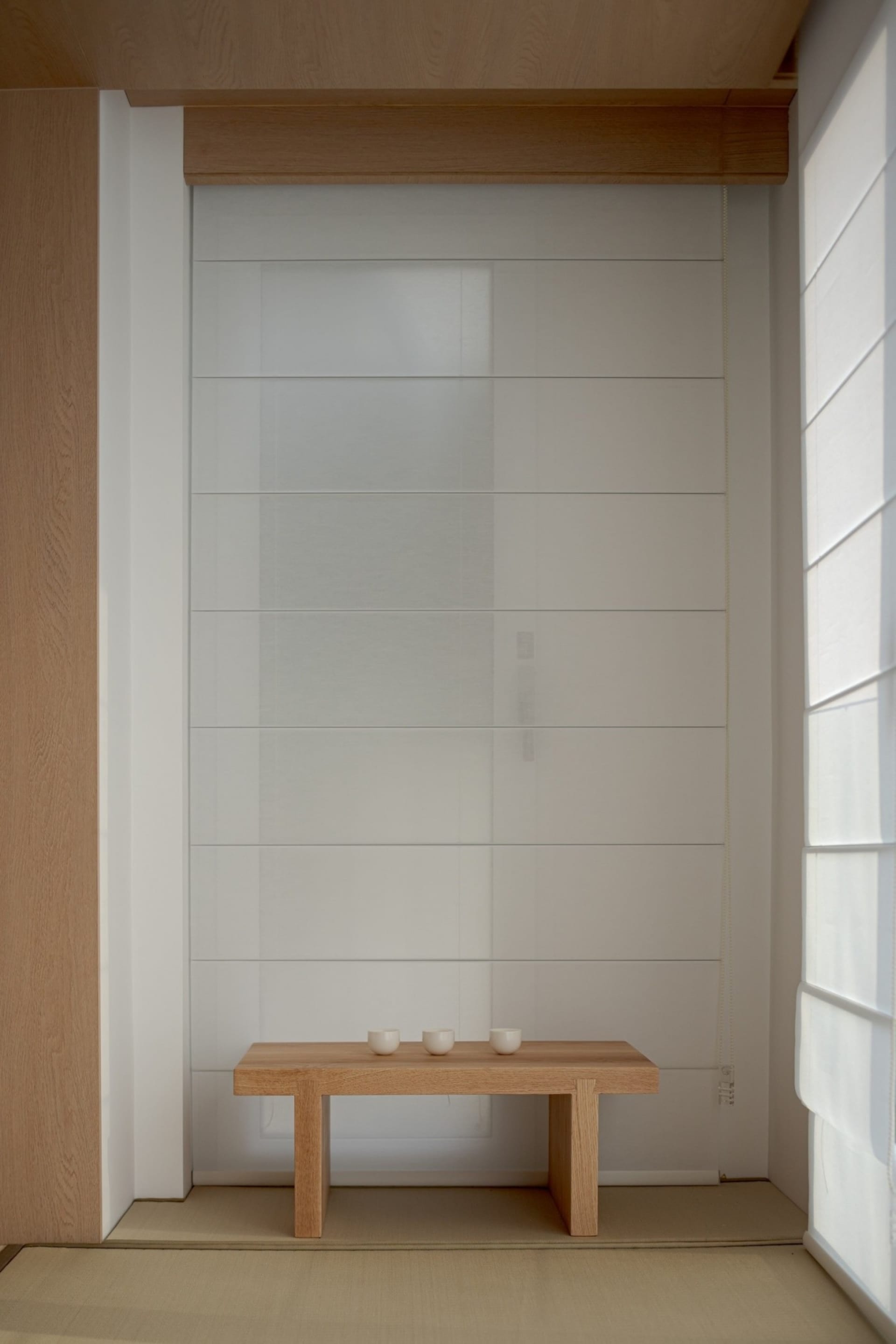 A minimalist tea ceremony setting featuring wooden furniture and three small cups on a wooden table.