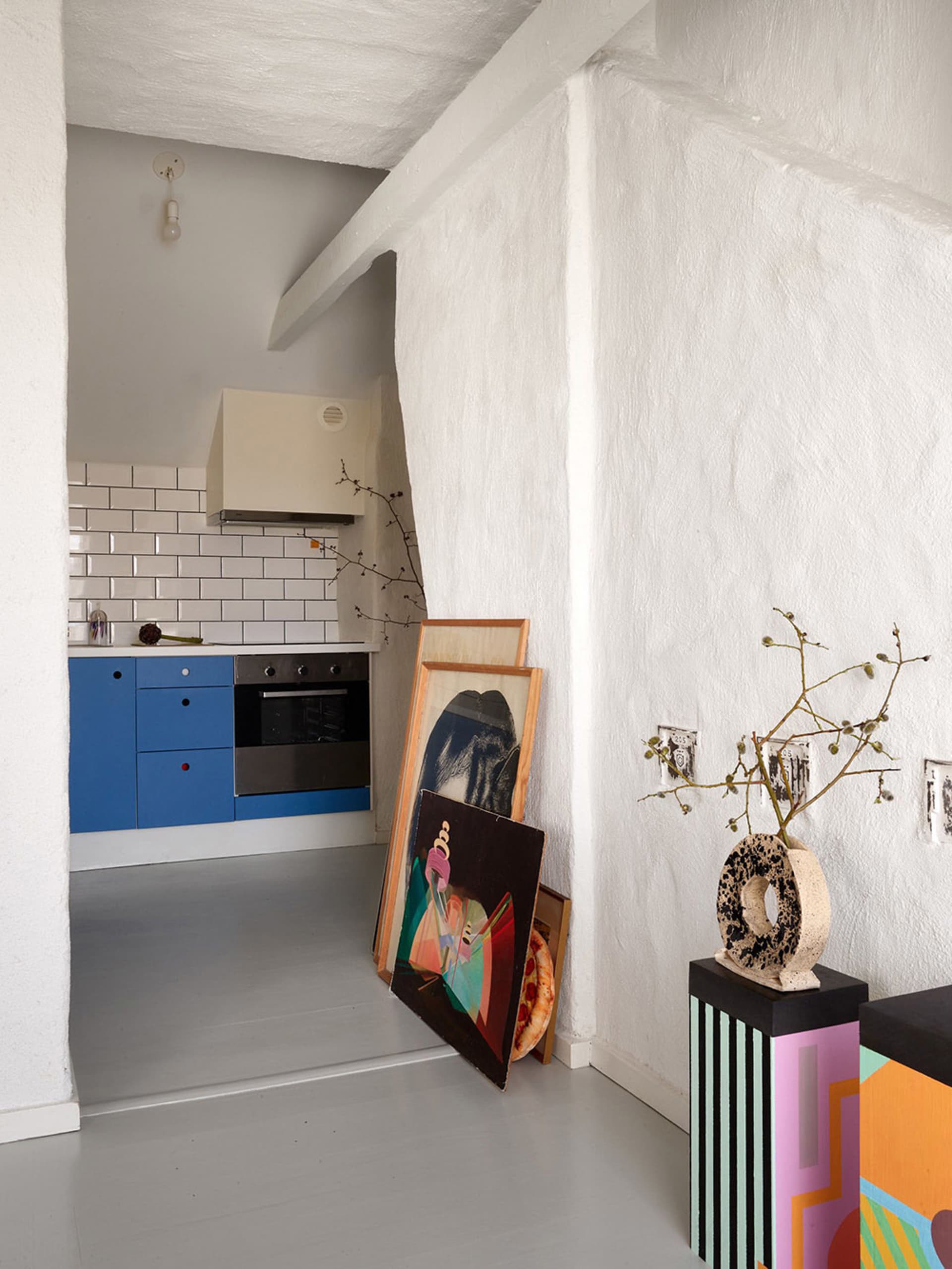 A modern kitchen with white painted walls, blue cabinets, and framed artwork leaning against the wall.