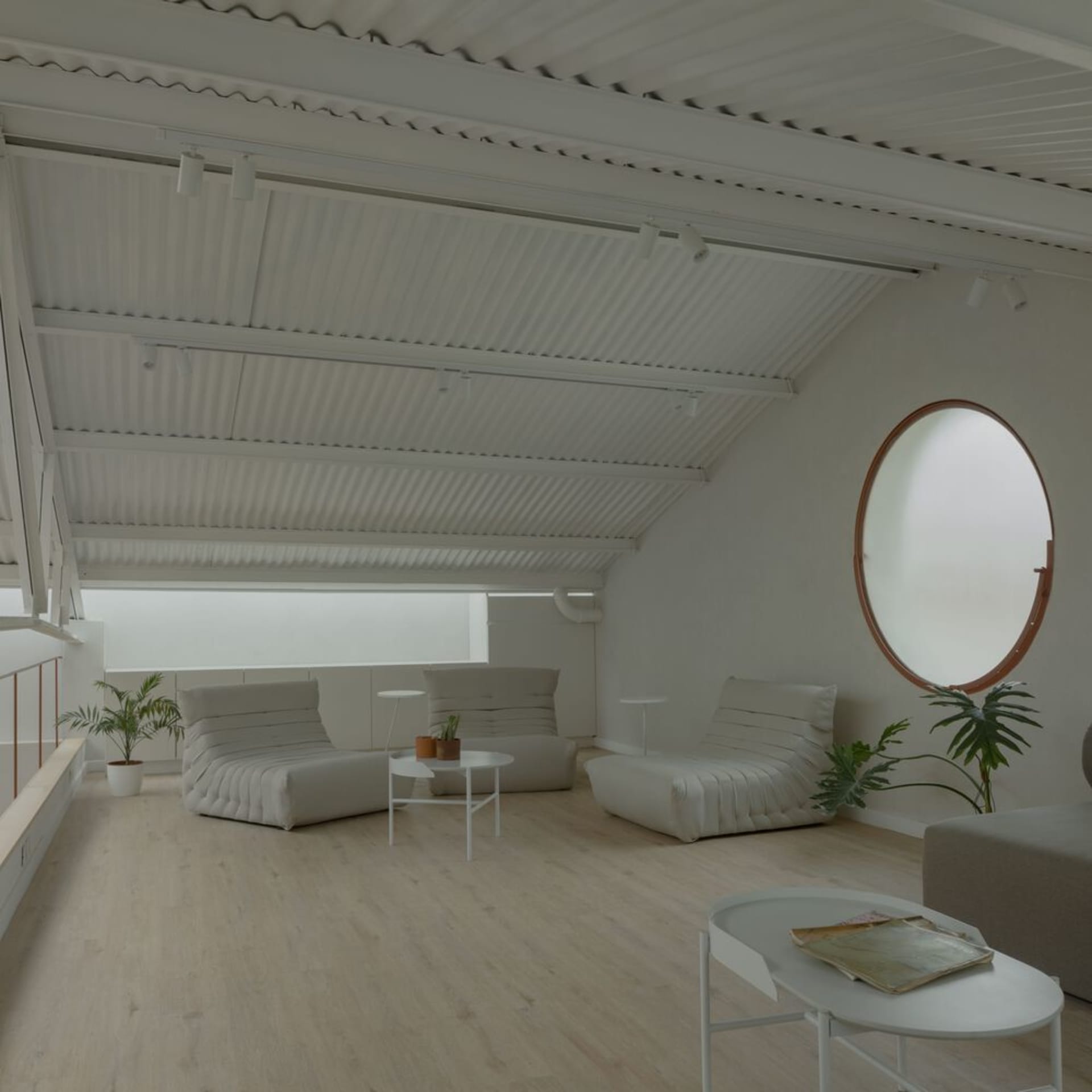 A minimalist living room with neutral-colored furniture and decor, featuring a large round window and a slanted ceiling.