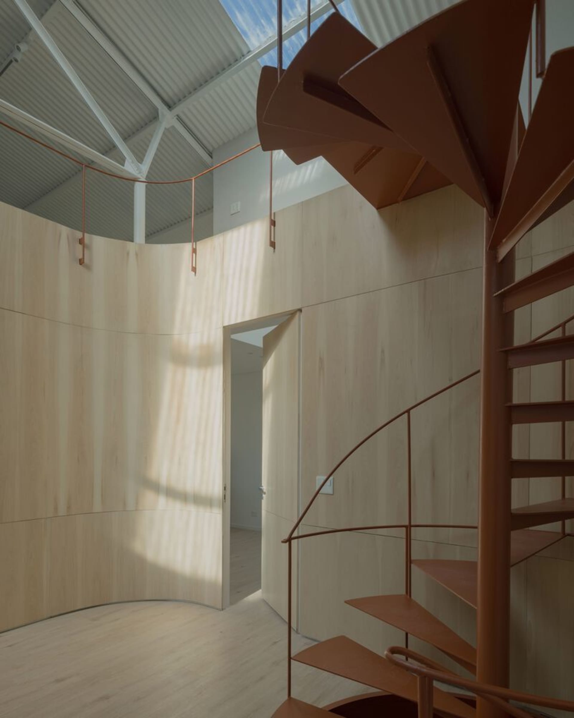 Modern, minimalist interior design featuring a wooden spiral staircase with metal railings.