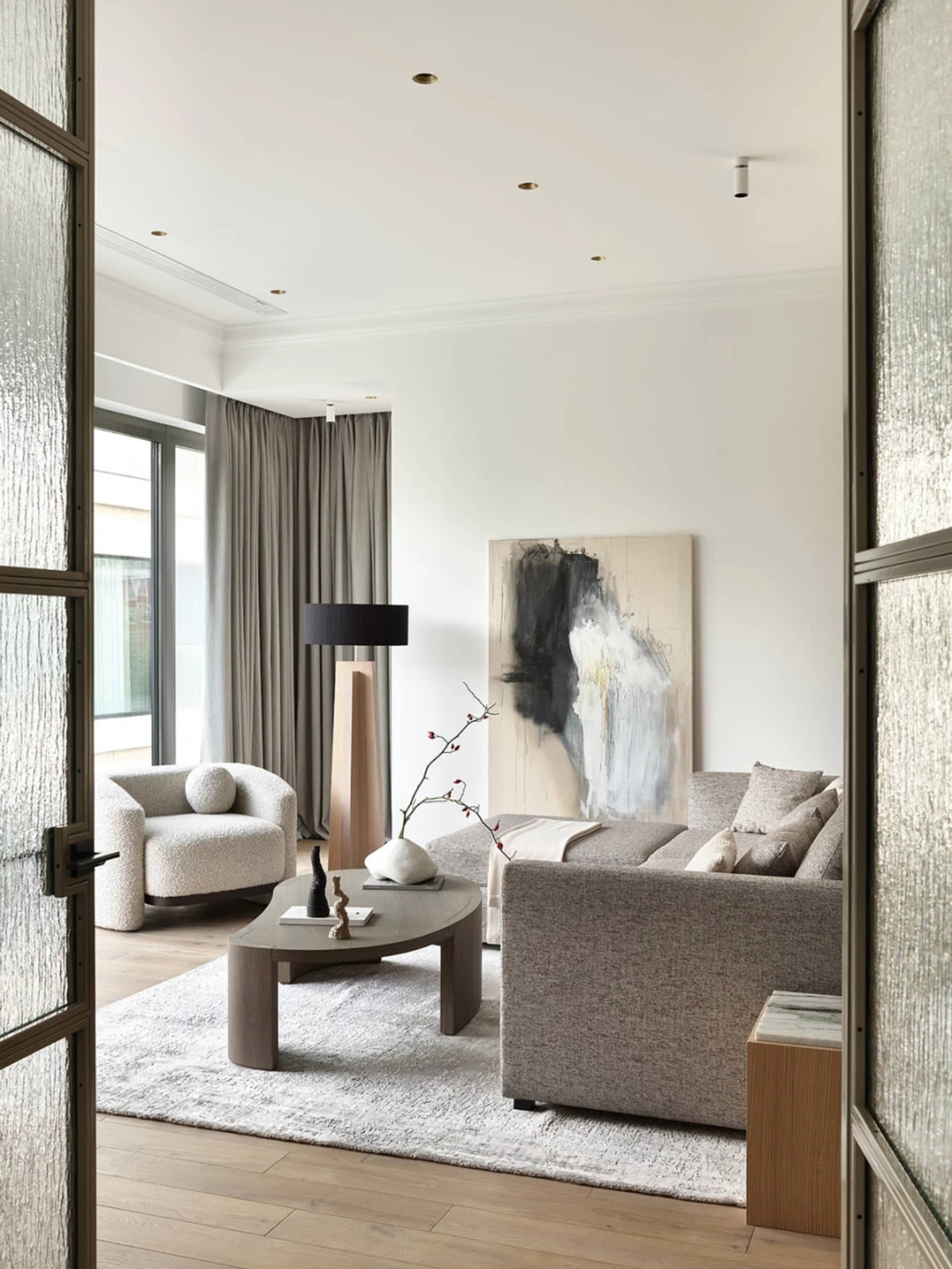 Modern living room with neutral-toned furniture, minimalist decor, and a large abstract painting.