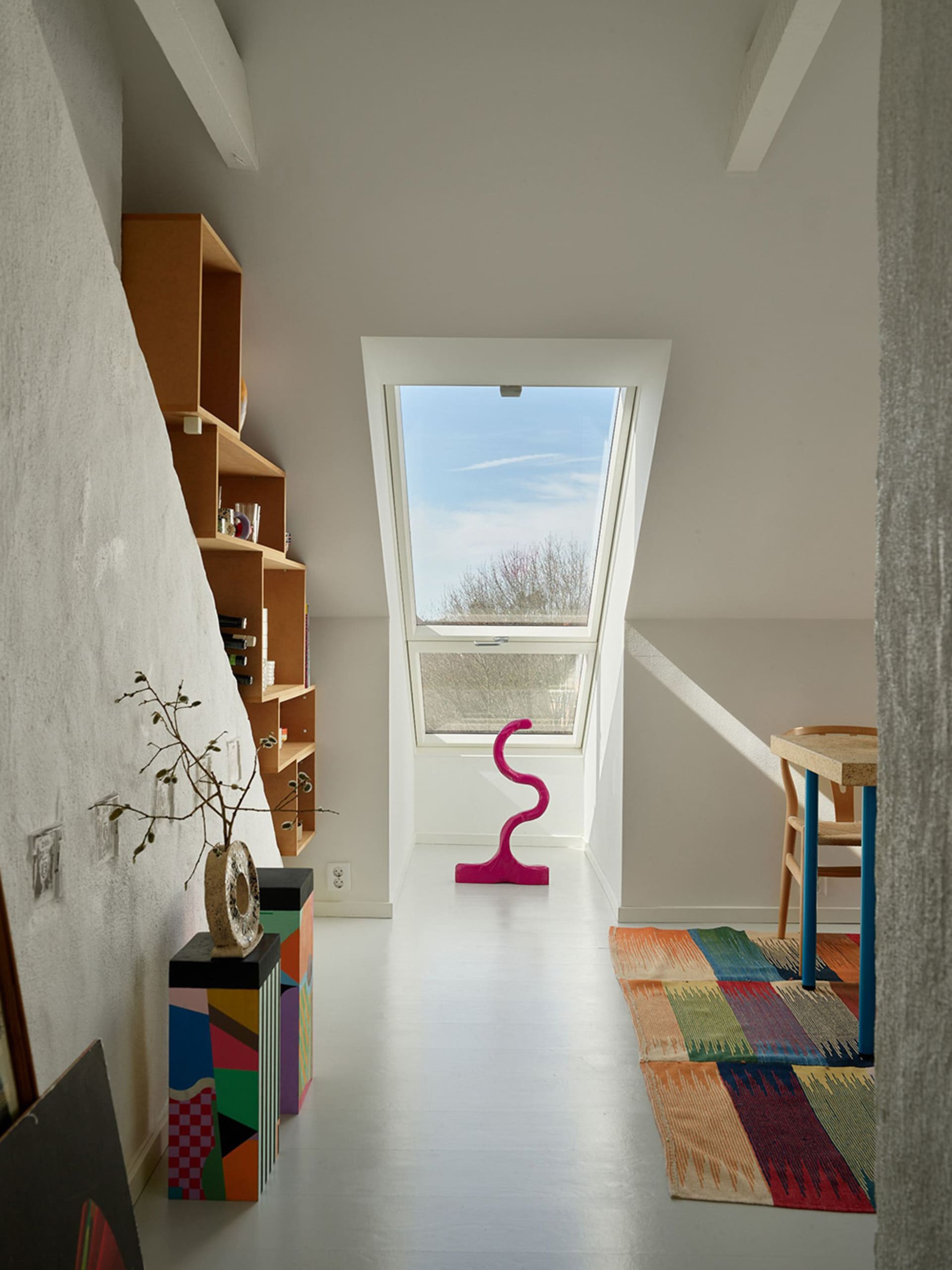 Modern residential space with a skylight, bookshelf, colorful rug, and abstract sculpture.