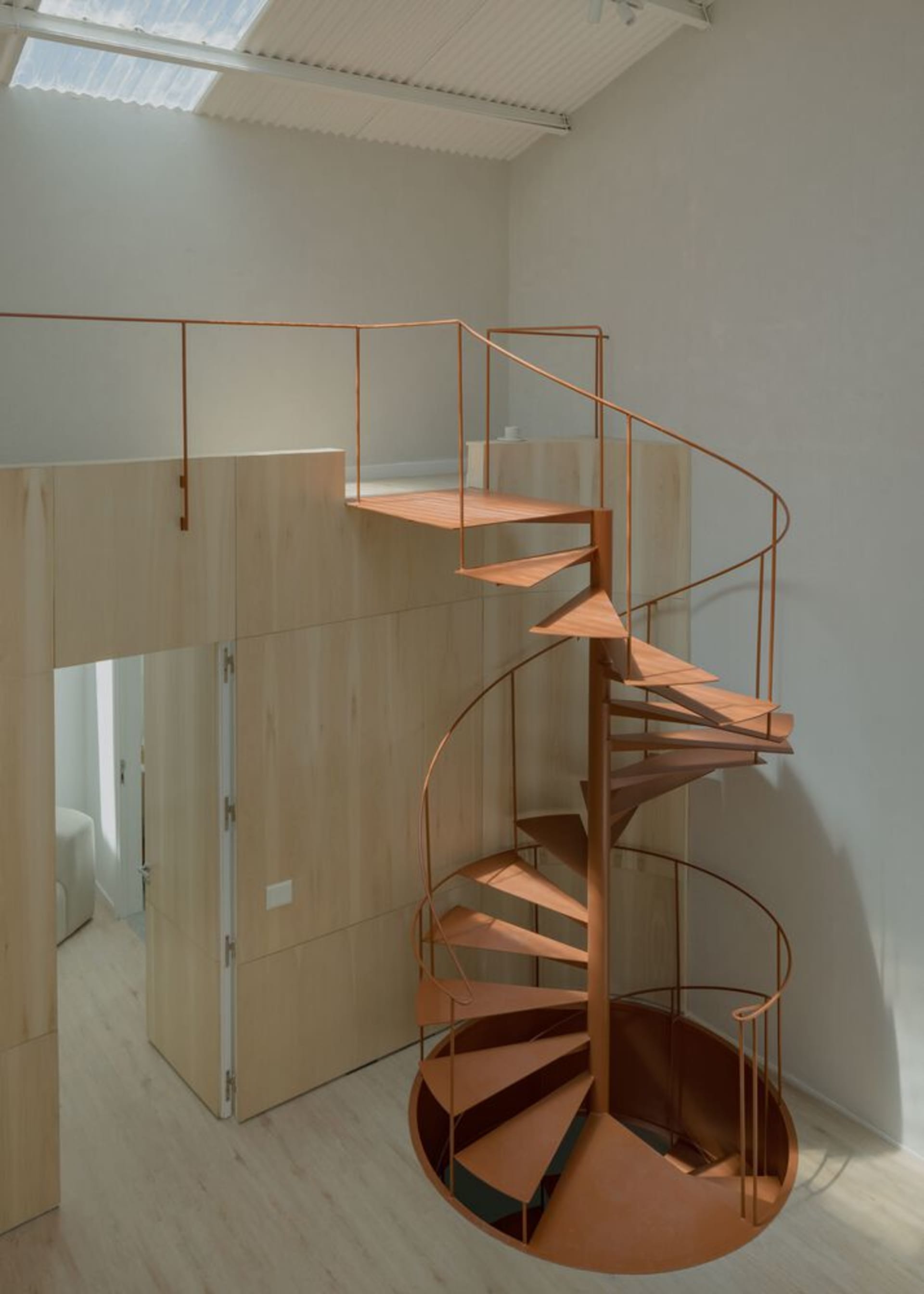 A modern, rotating staircase made of metal in a minimalist interior space.