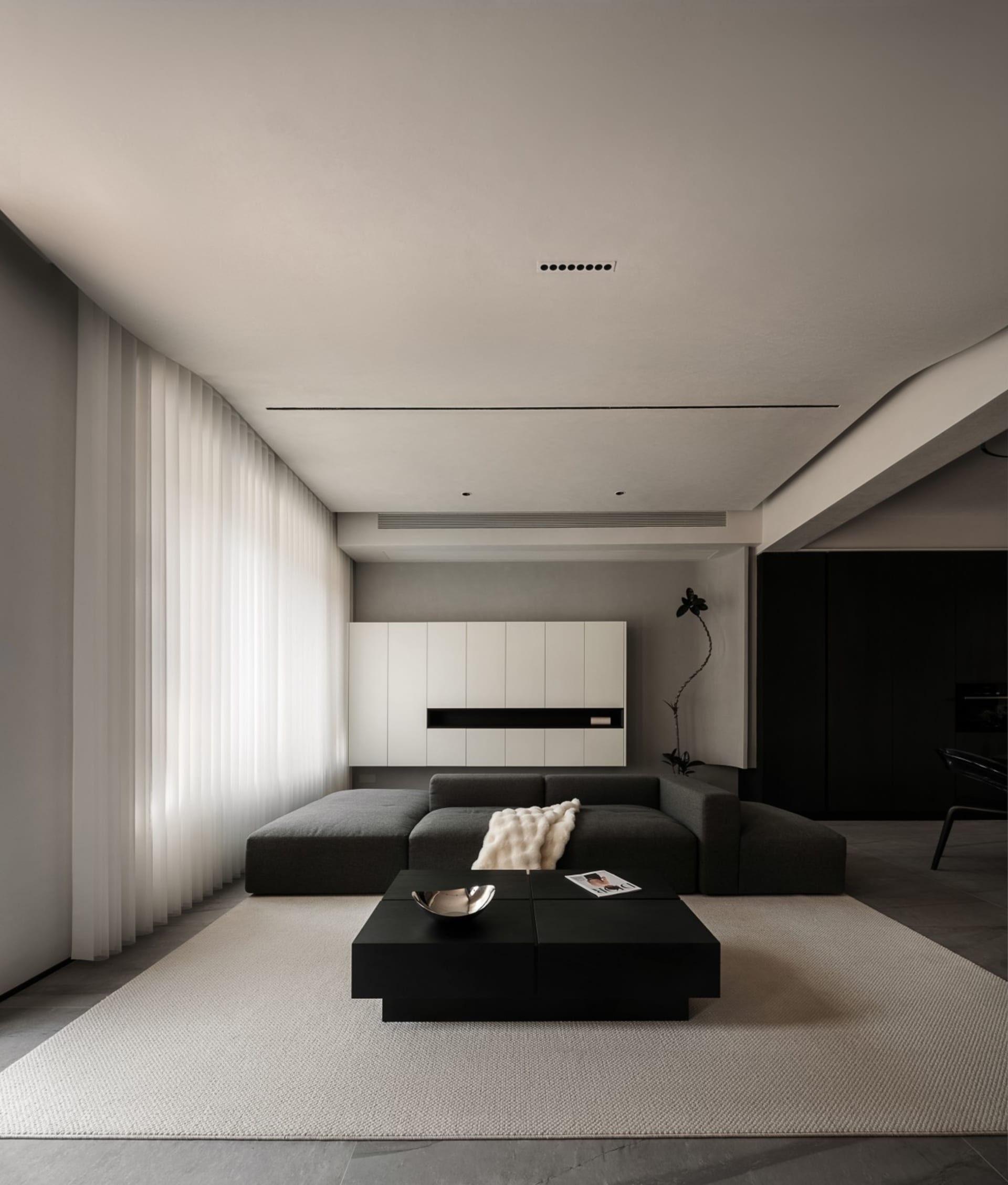 A minimalist living room with a fabric sofa, black coffee table, and white curtains.