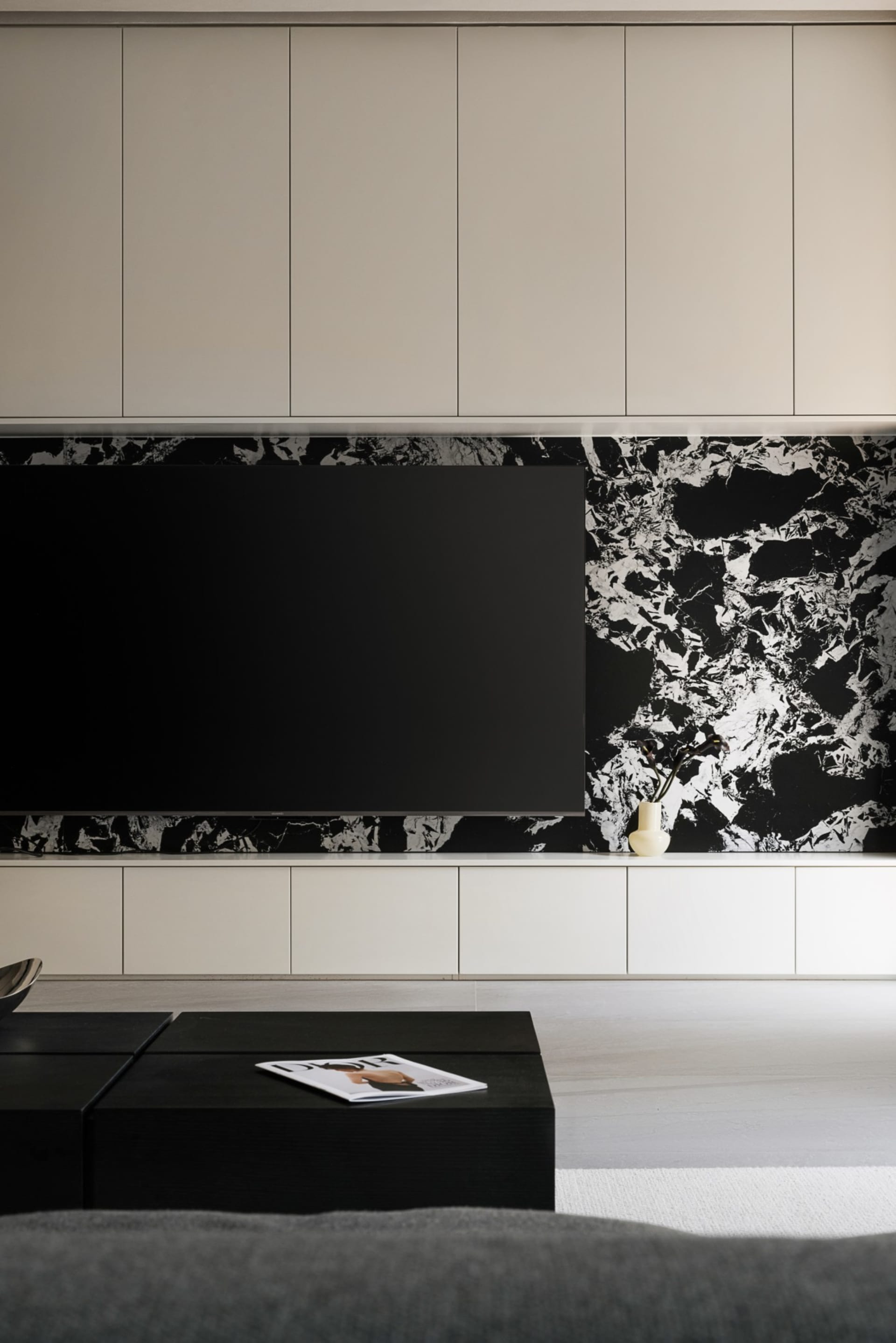 A modern minimalist living room featuring a large black flat-screen TV mounted on a black and white marble wall with a white