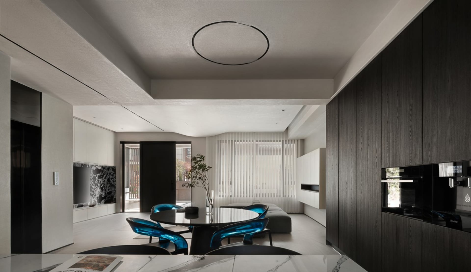 A modern living-dining room with mixed materials, featuring sleek black furniture, teal chairs, and a round table.