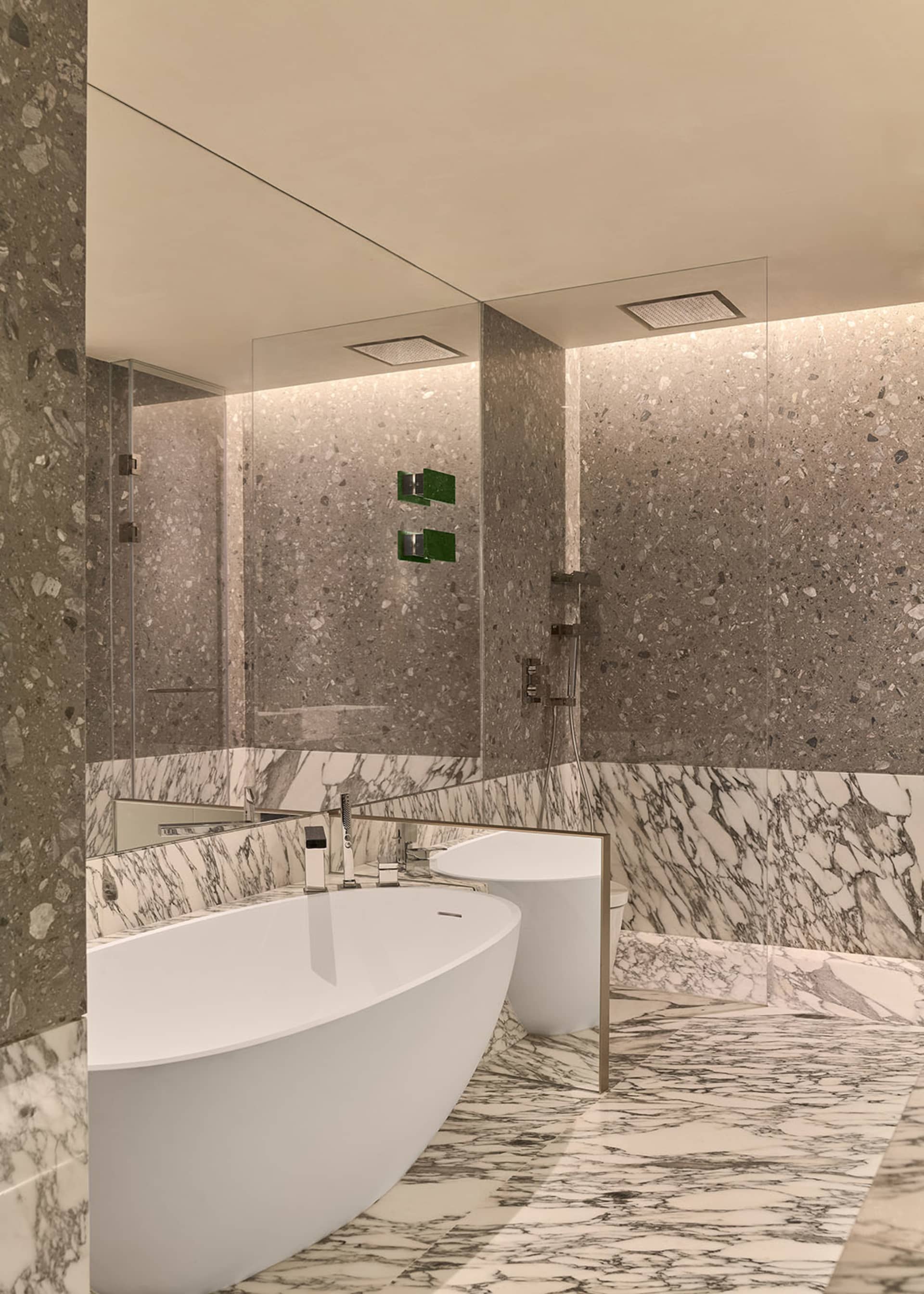 A contemporary bathroom with marble countertops and a glass bathtub.