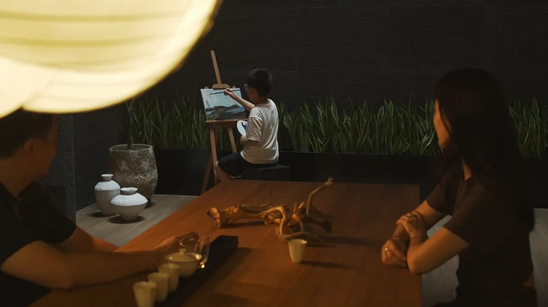 A minimalist family room setting with a young person painting at an easel, while two adults sit at a dining table observing.