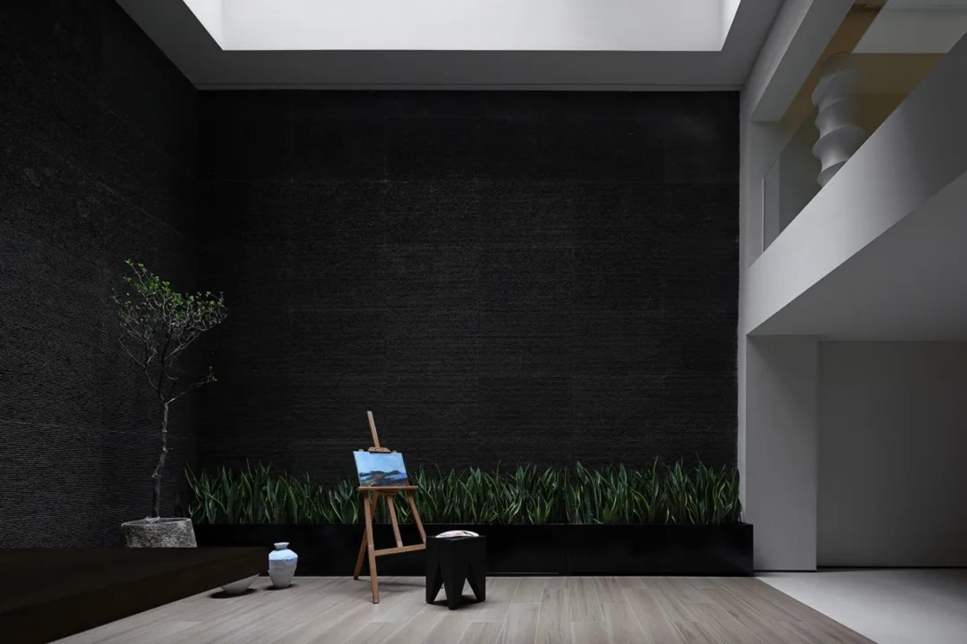 Modern living room featuring a dark textured wall, a small tree, and a painting on an easel.