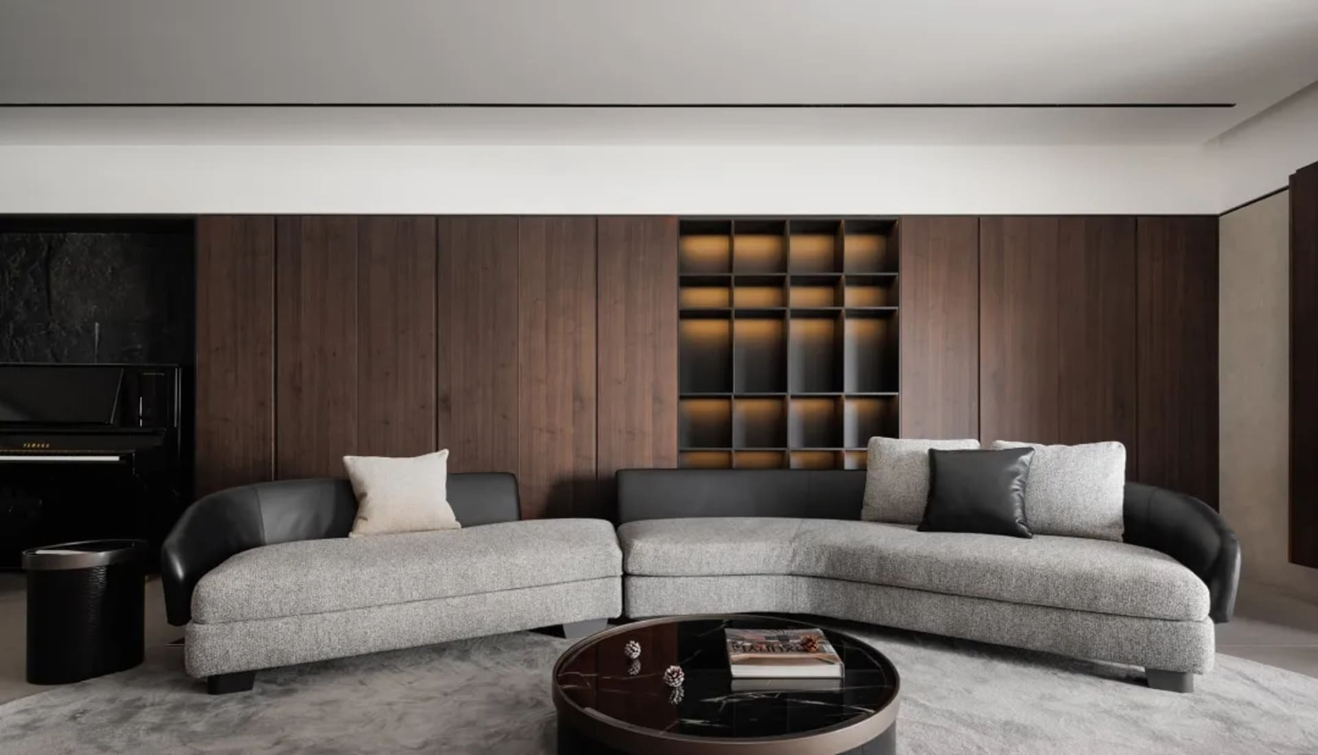 Modern living room with a curved gray sofa, white and black pillows, dark wood panels, and a round black coffee table on a li