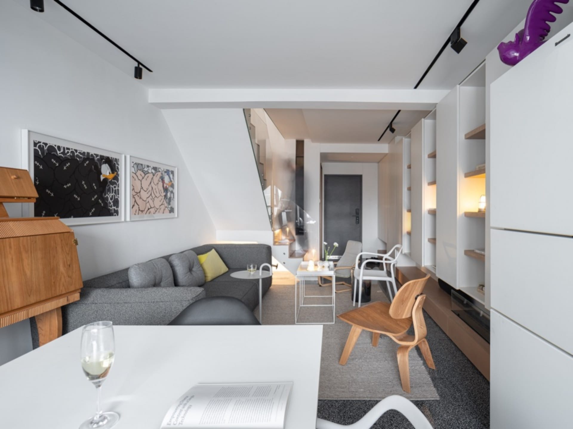 Modern living room with a sleek, grey sectional sofa adorned with soft yellow accents, set against a backdrop of minimalist w