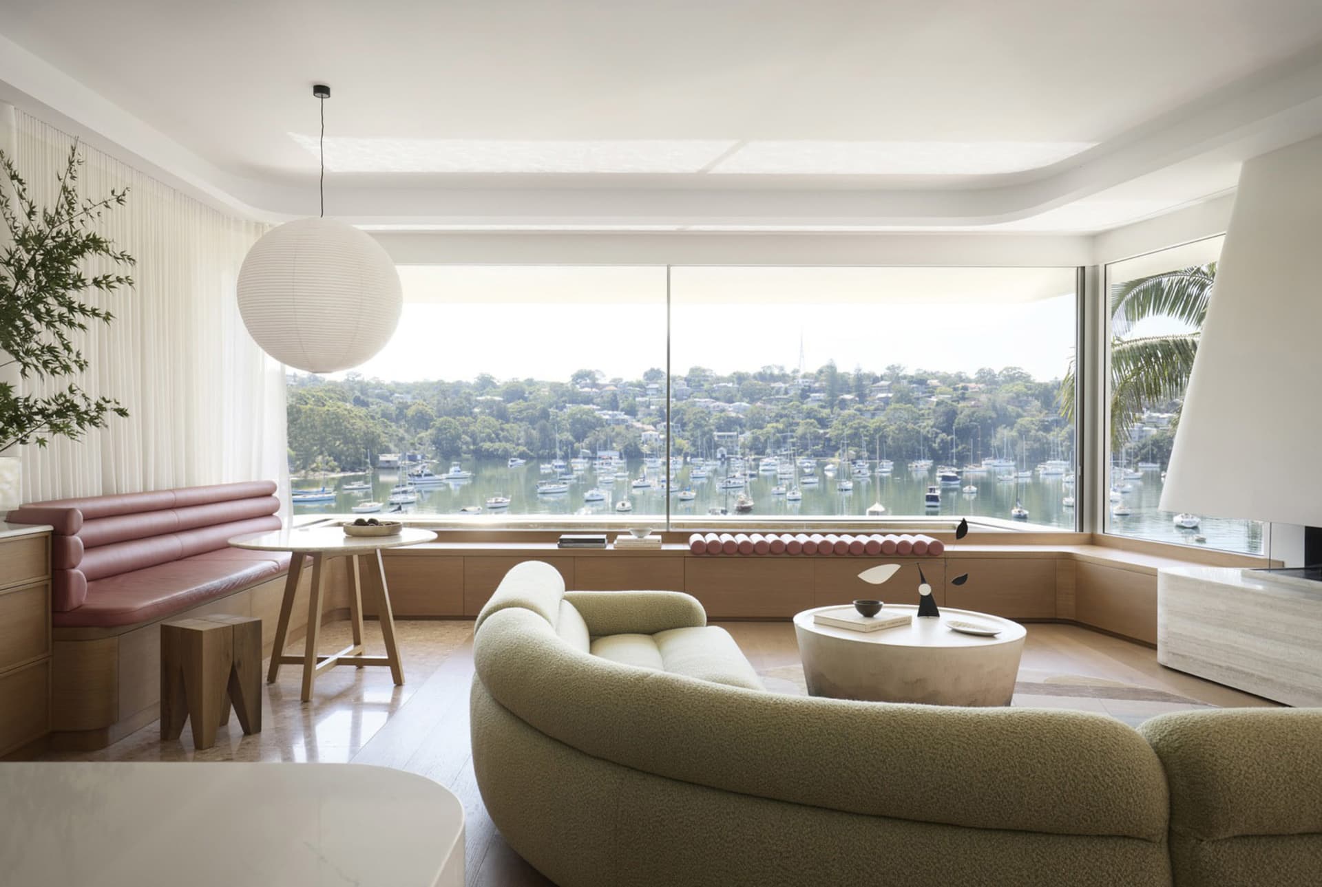 Modern living room featuring a wooden floor, glass windows overlooking a marina, and a large curved sofa with a round coffee