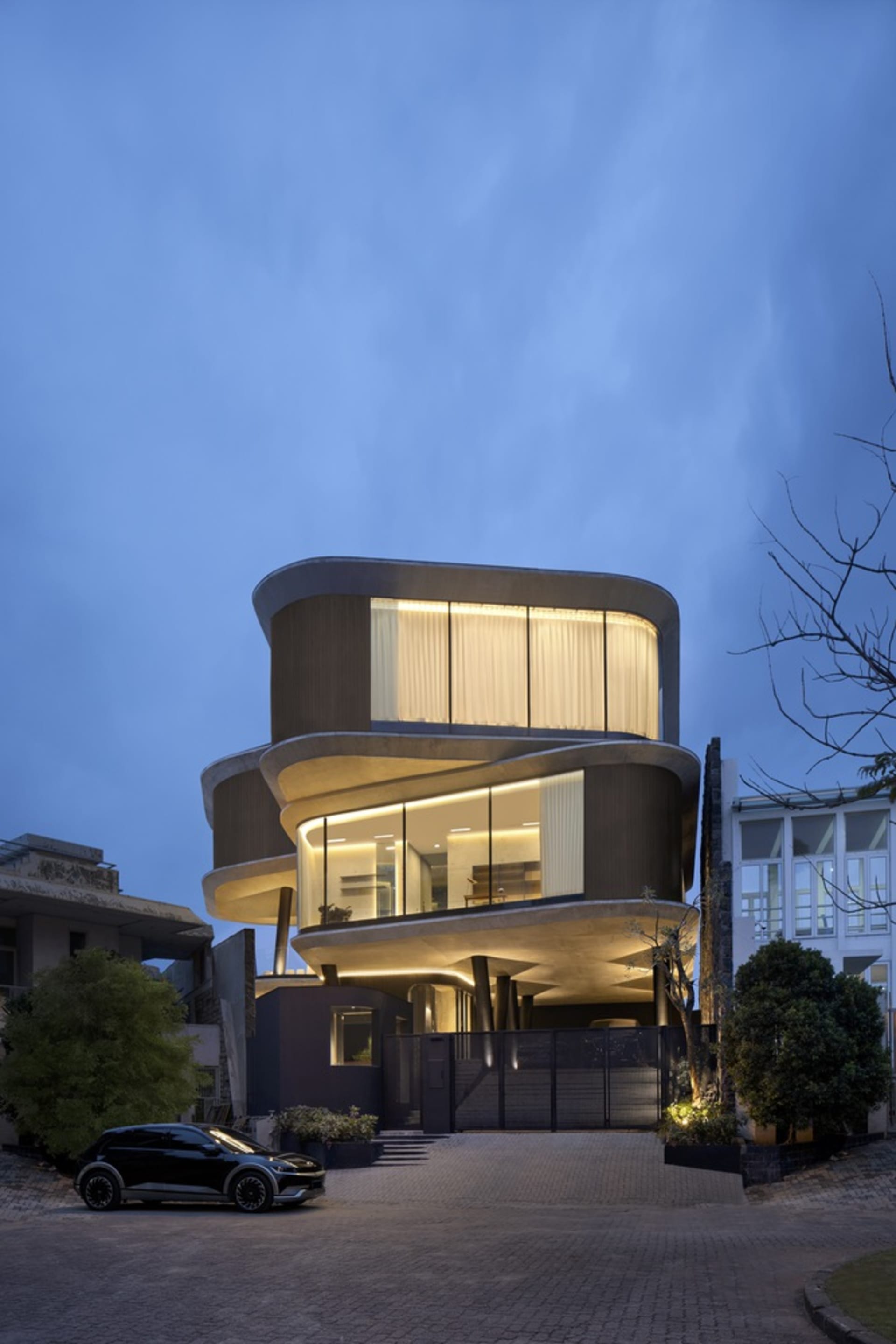 A modern concrete residential house at night illuminated with warm interior lights.