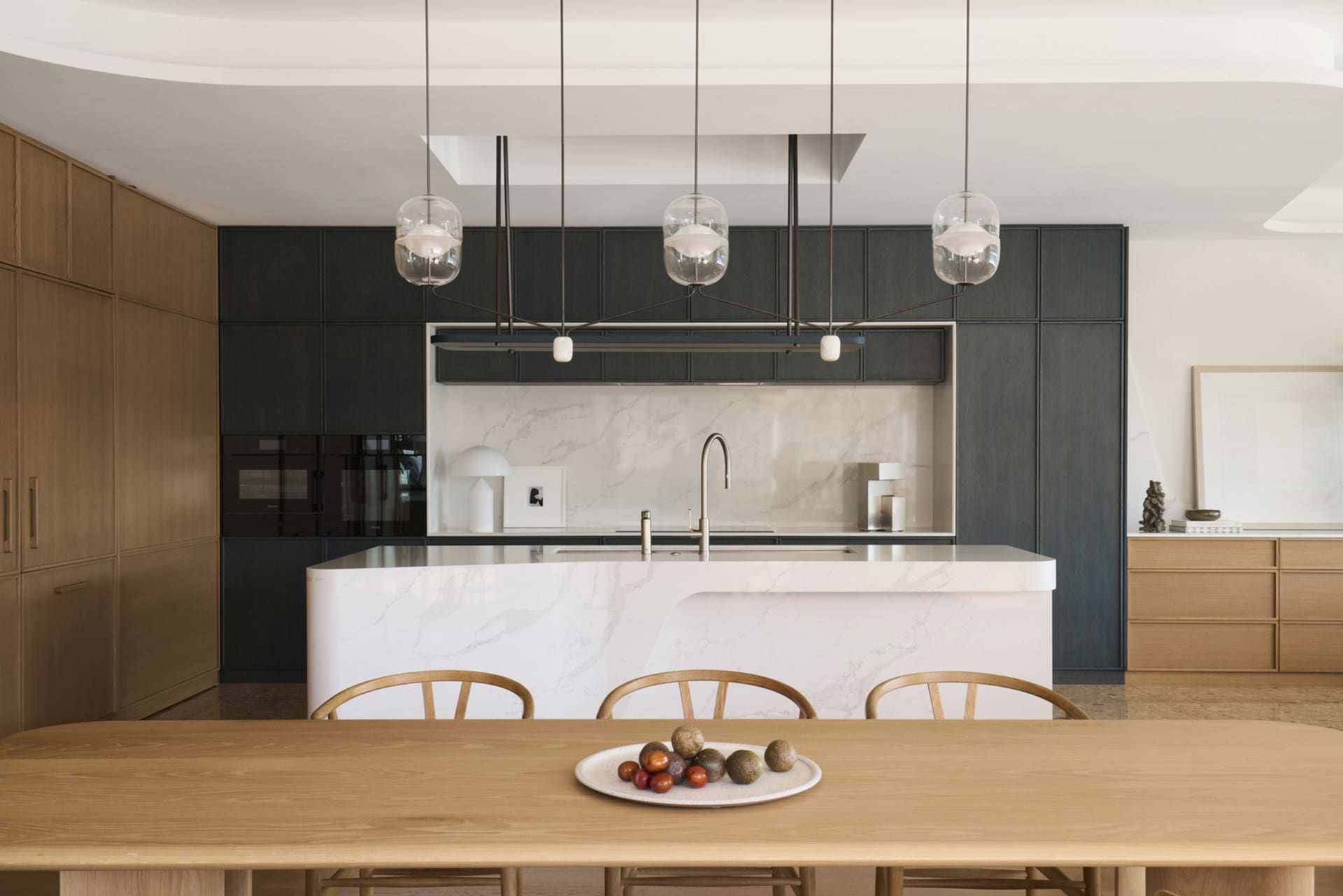 A modern, minimalist kitchen with a marble island and pendant lights.
