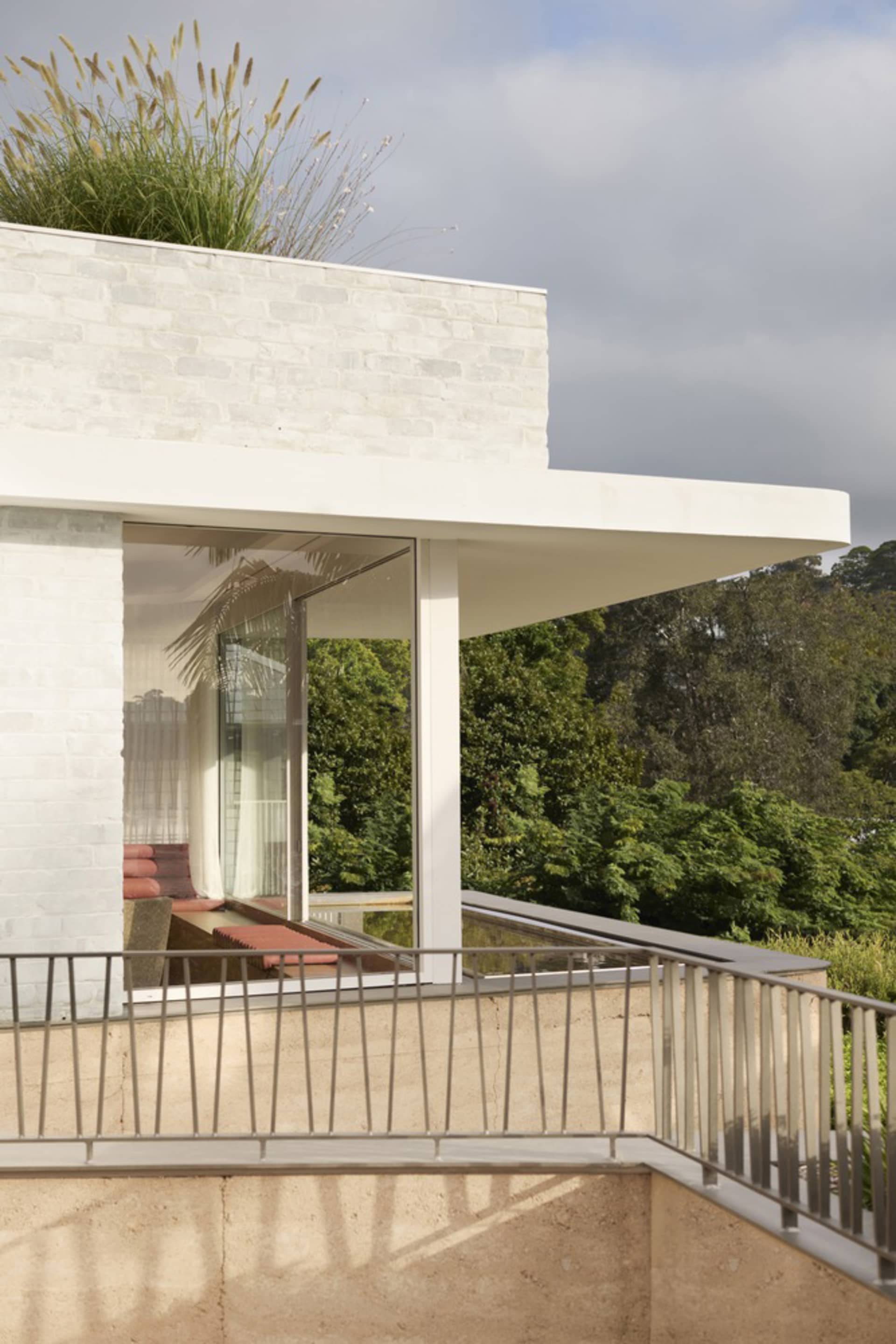 A modern residential building with a concrete exterior and glass windows, set against a backdrop of greenery.