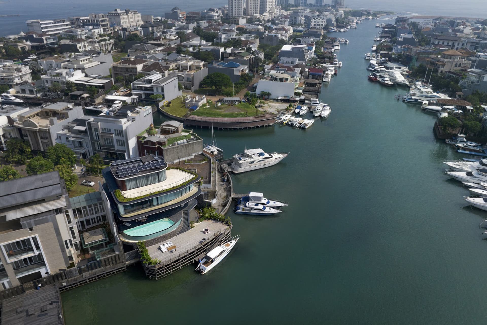 Aerial view of a waterfront development featuring concrete, glass, and timber structures with a pool and marina.
