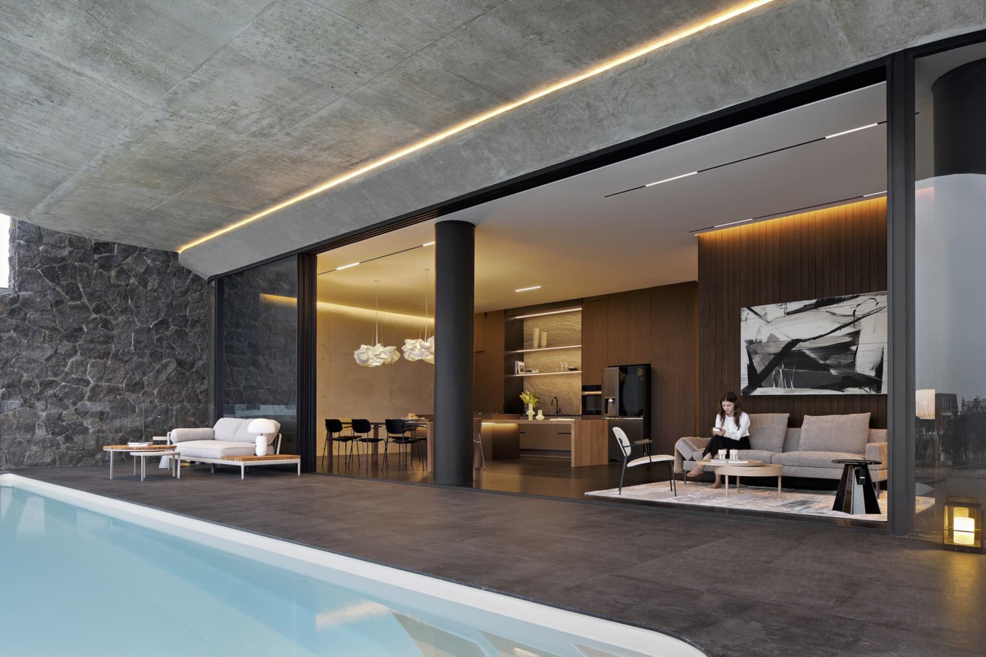 A modern living room with concrete walls and floor, featuring a sofa, coffee table, and illuminated ceiling lights.