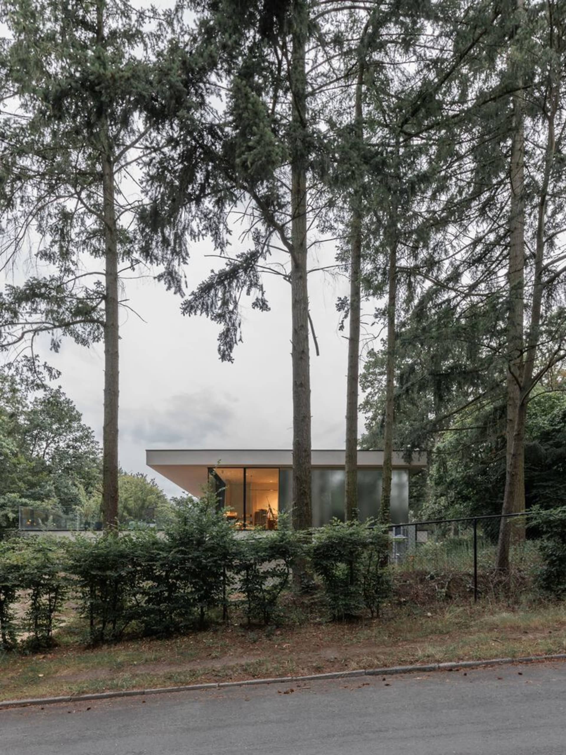 Modern house with glass and concrete exterior and interior lighting visible through large windows.