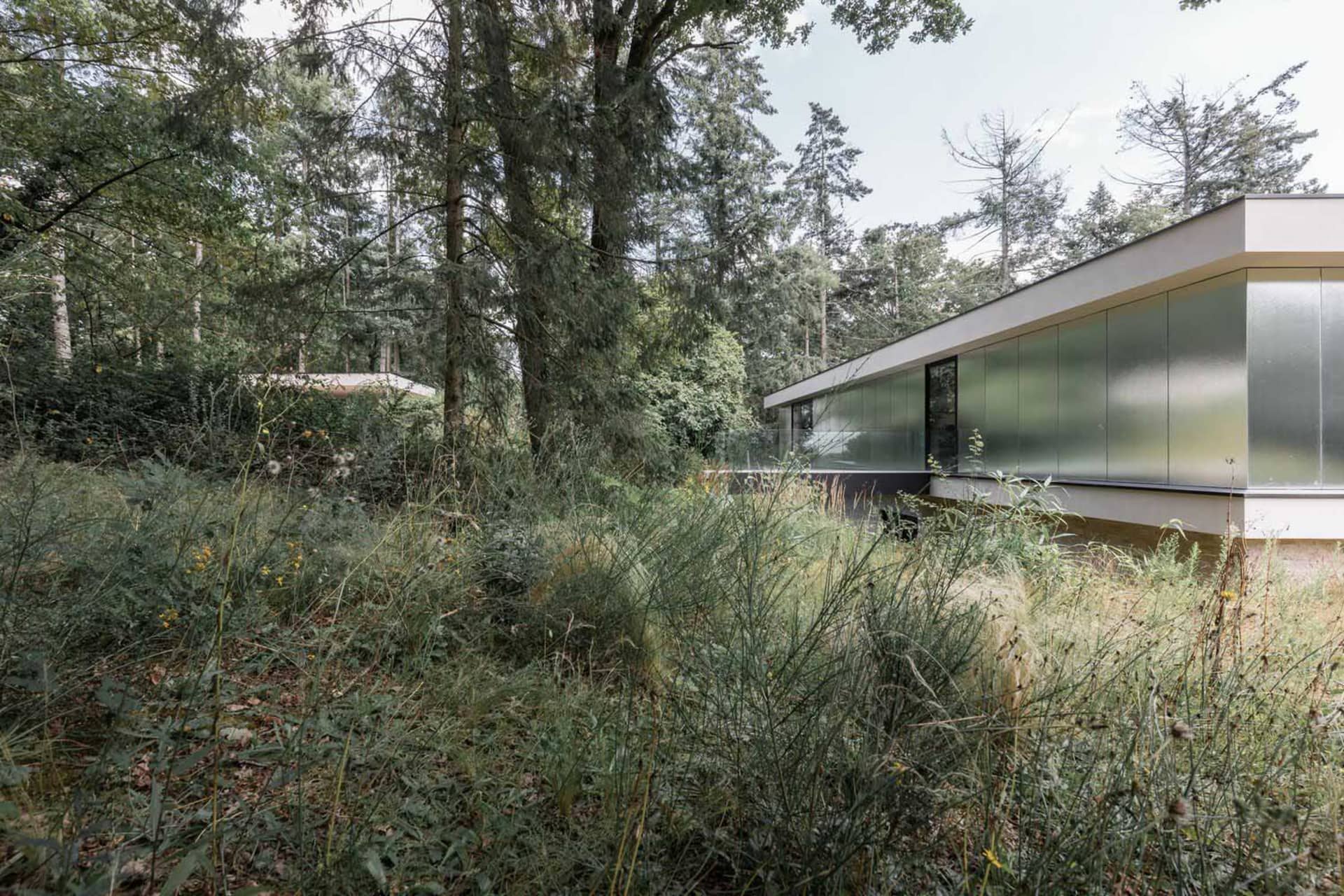 Modern house with metallic and glass exterior in a wooded area.