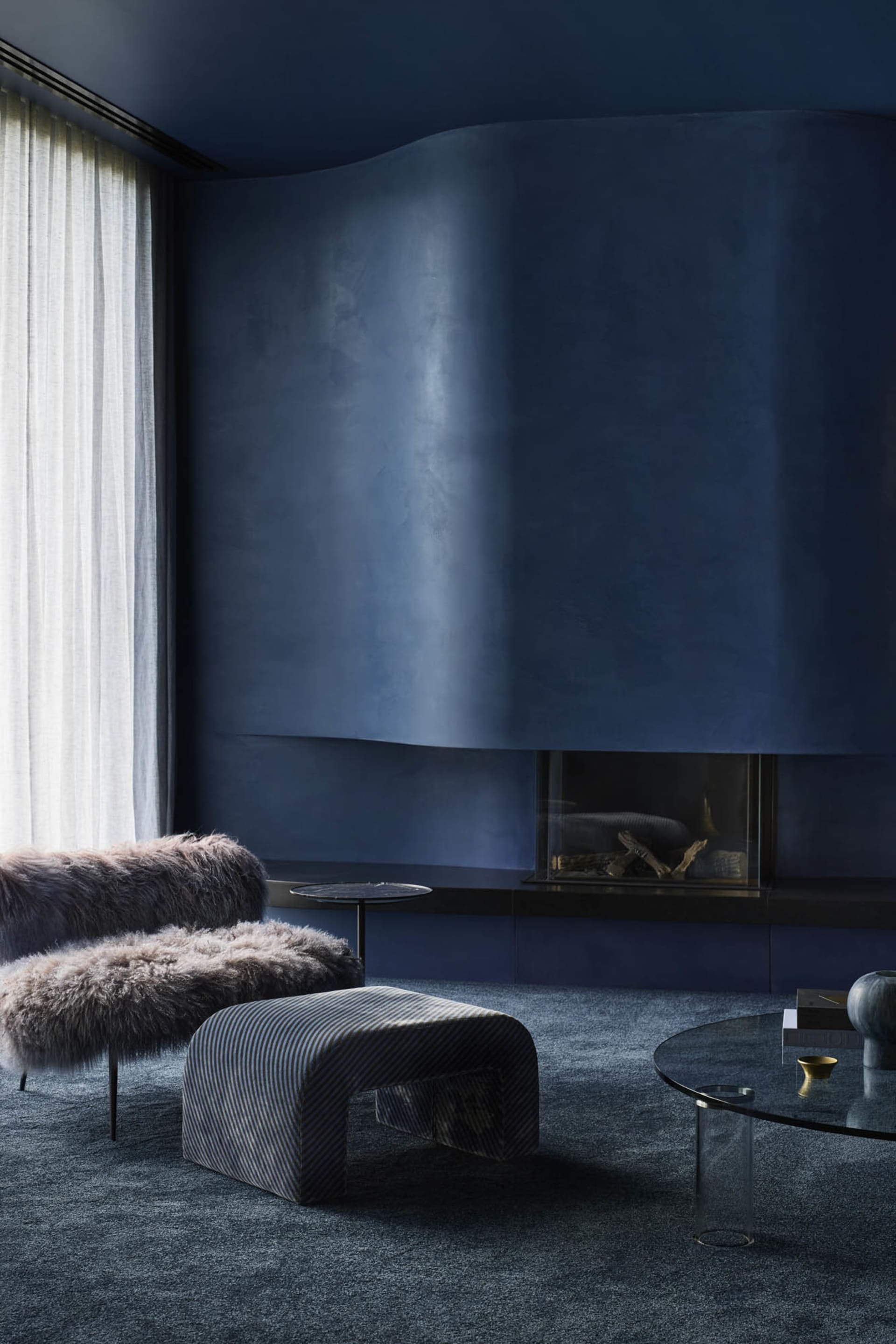 A modern industrial living room features plush, fur-covered seating and a sleek, glass-top coffee table with minimalist decor