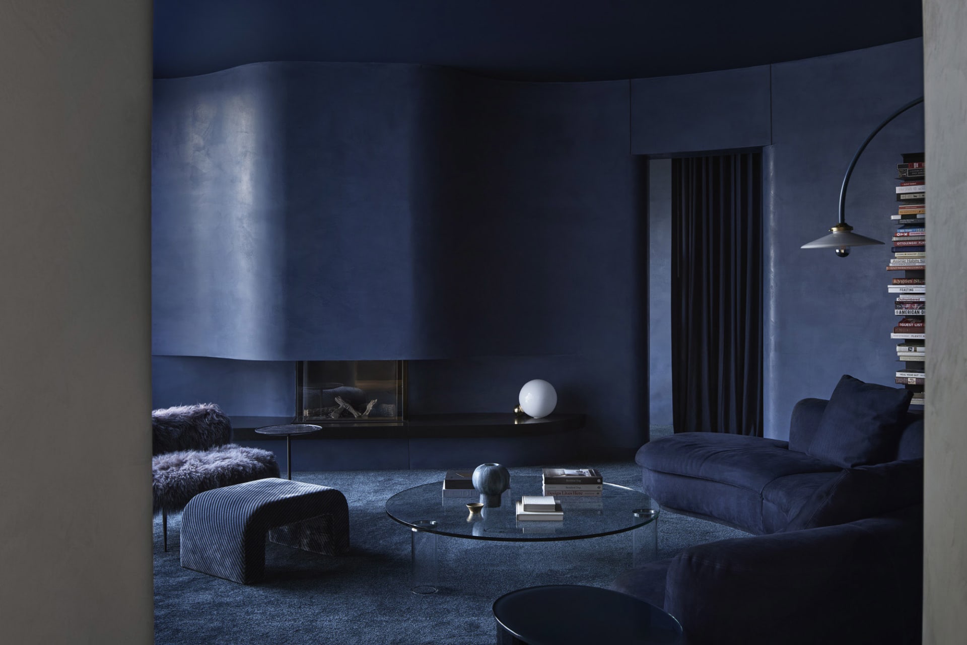 A modern minimalist living room with textured concrete walls and a dark blue color scheme, featuring a round glass coffee tab