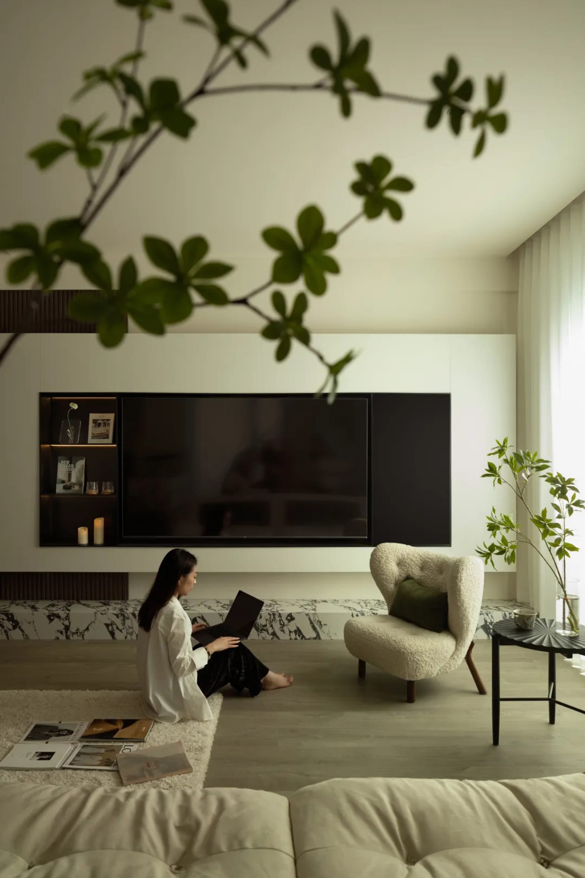 A modern living room with a marble accent wall, white furniture, and greenery.