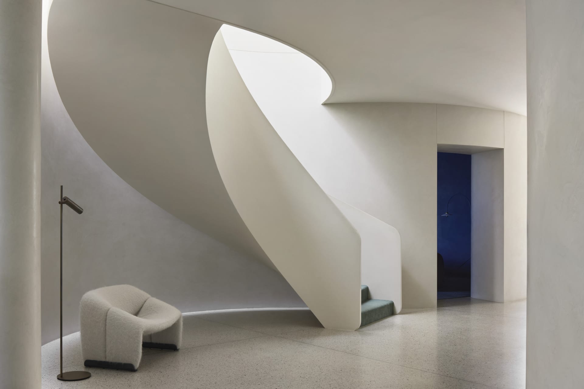 A modern living room with curved concrete walls and stairs.