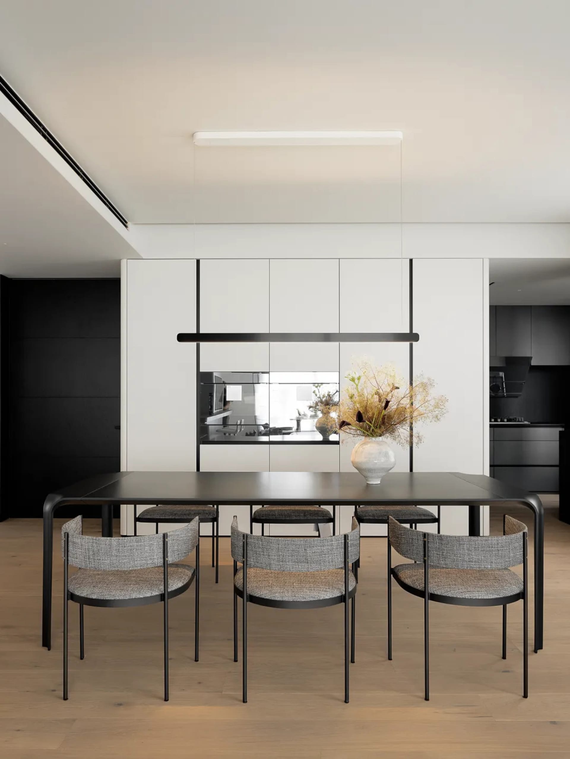 Modern minimalist dining room with metal table, wood flooring, and textured fabric chairs.