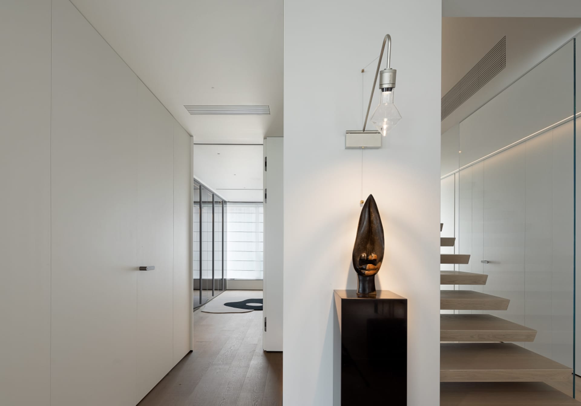 A modern residential staircase featuring glass railings and wooden steps, with minimalist decor and sleek lighting fixtures.