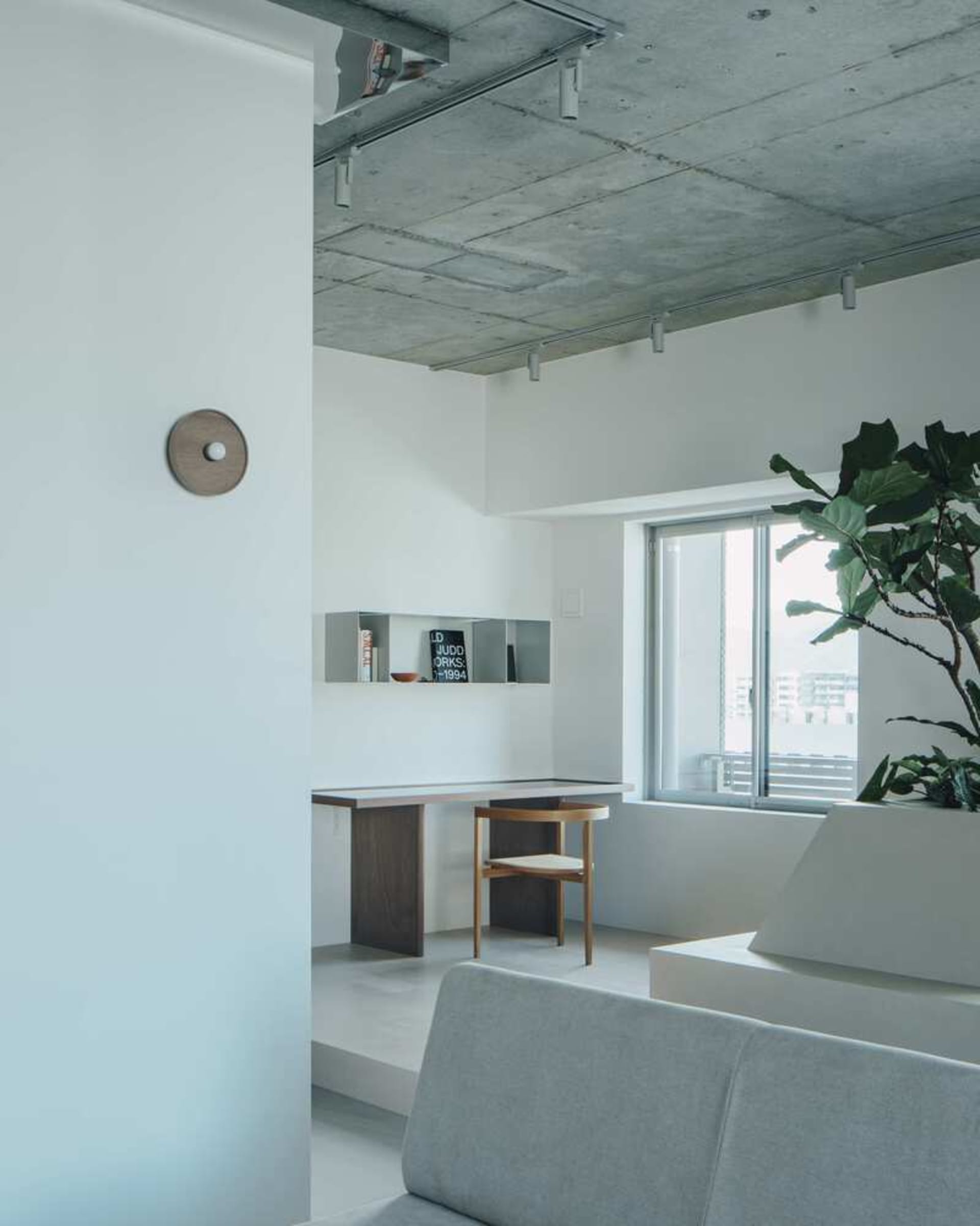 Minimalist residential interior with exposed concrete ceiling, wooden furniture, and a green plant.